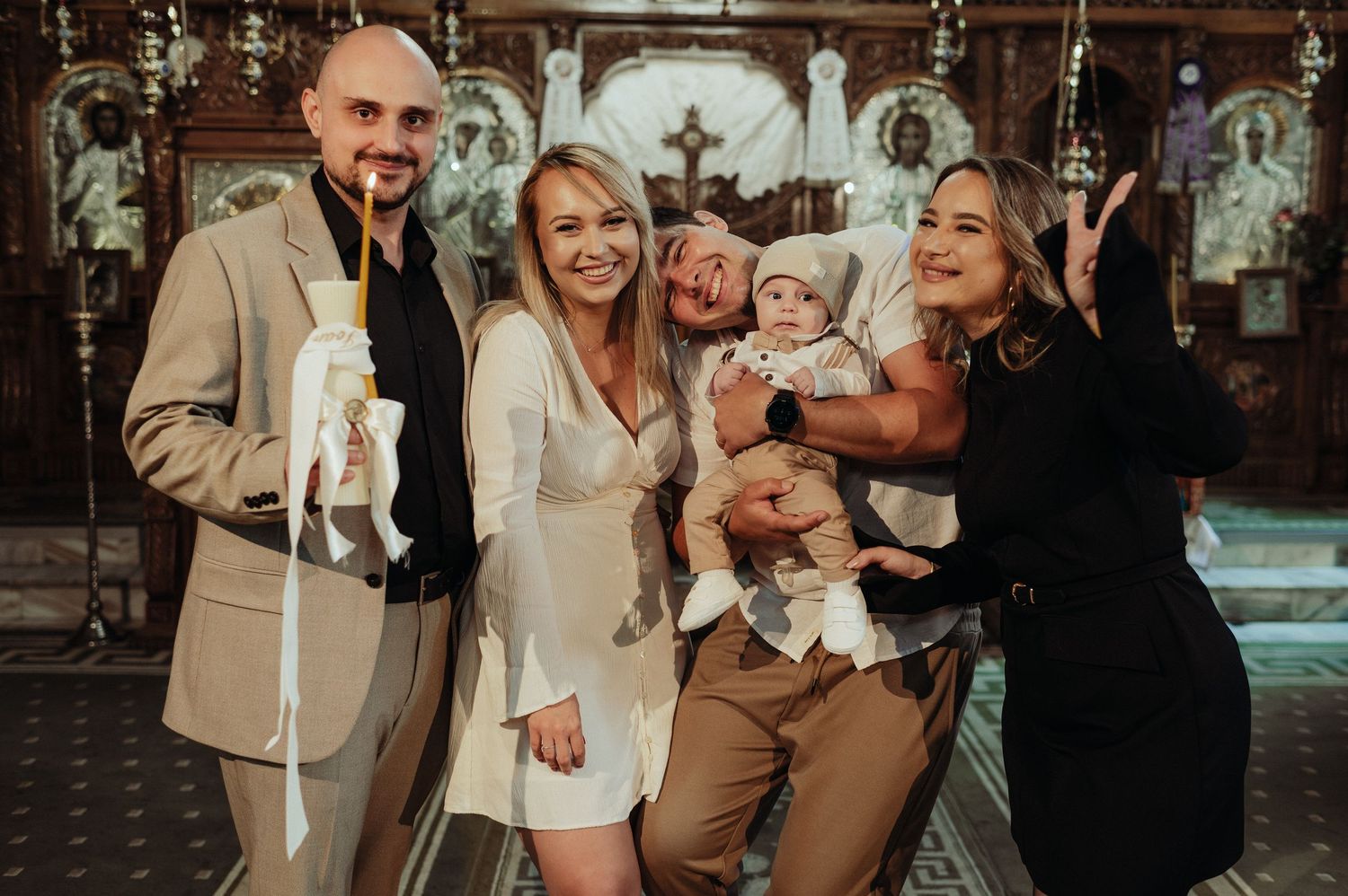 Happy family posing with a baby and baptism candle inside a beautifully decorated Orthodox church.