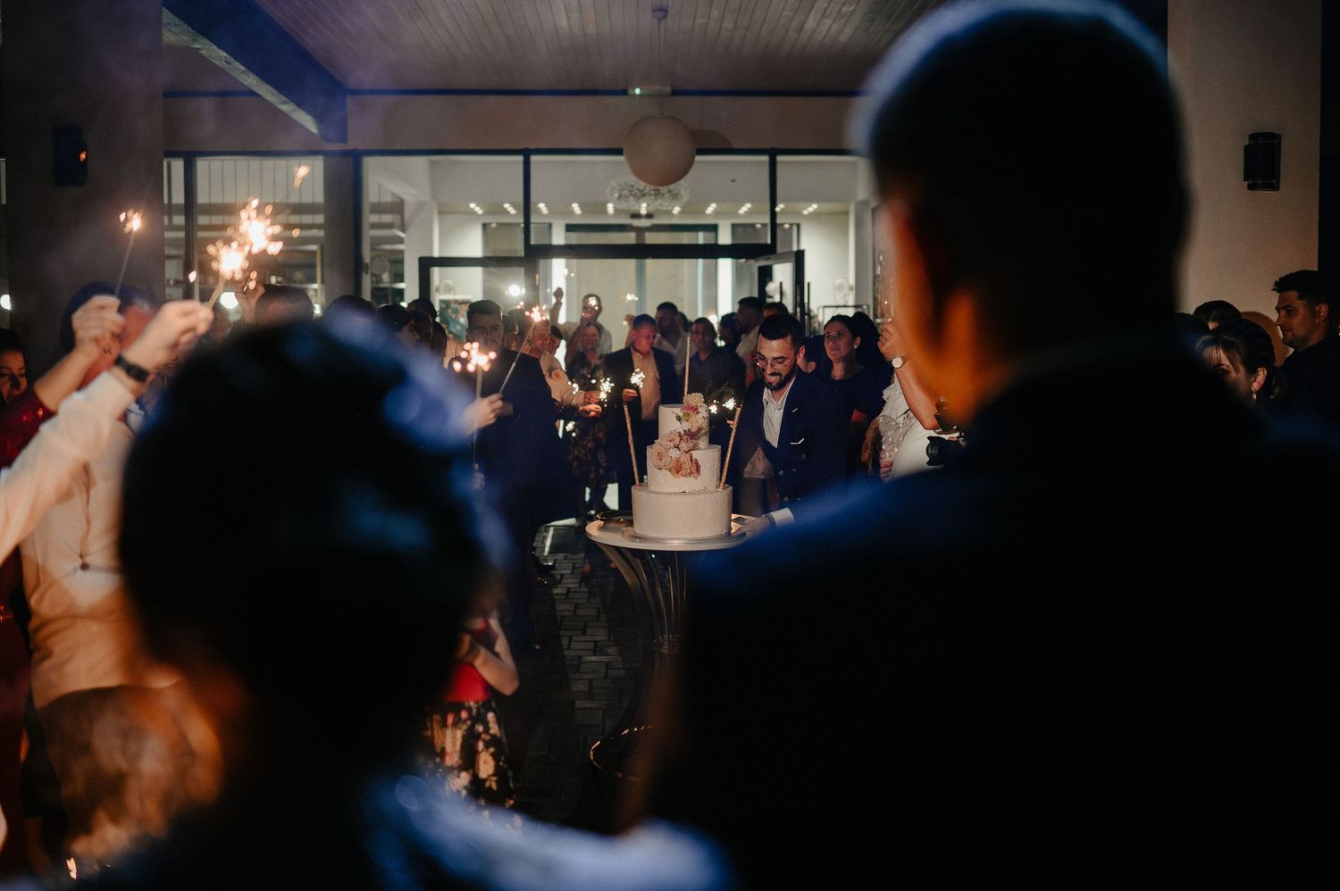 Guests celebrating with sparklers around wedding cake at reception.