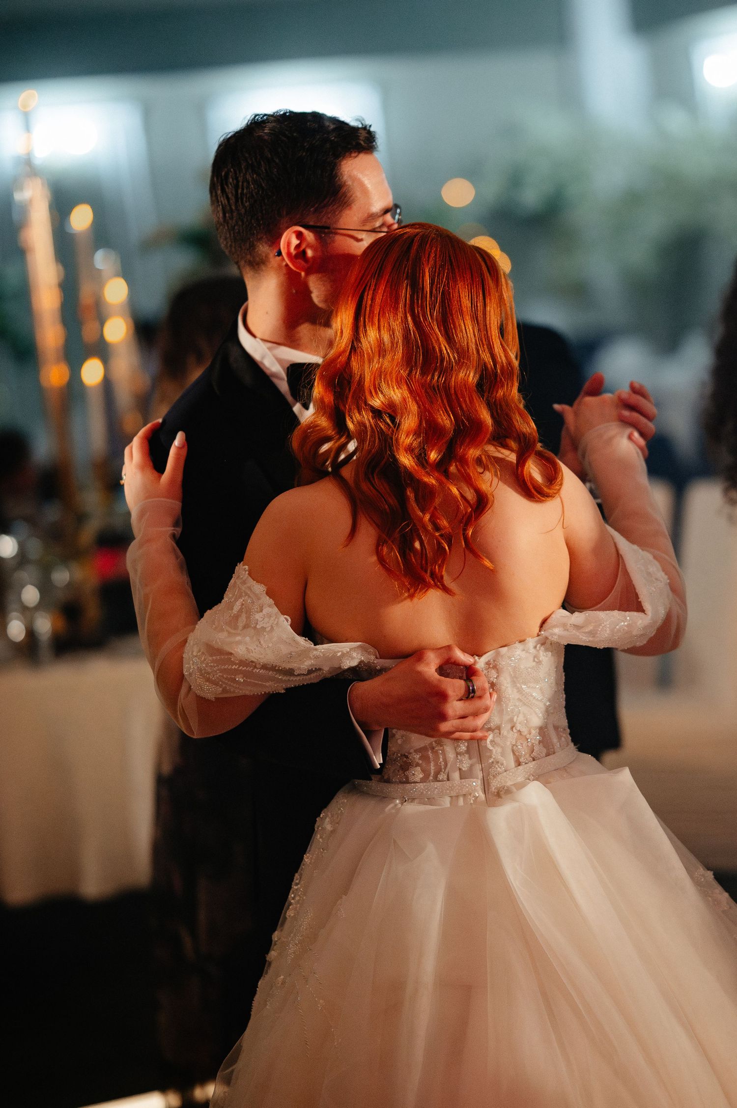 Bride and groom share their first dance, she in a white ballgown with red hair, he in a black tuxedo.