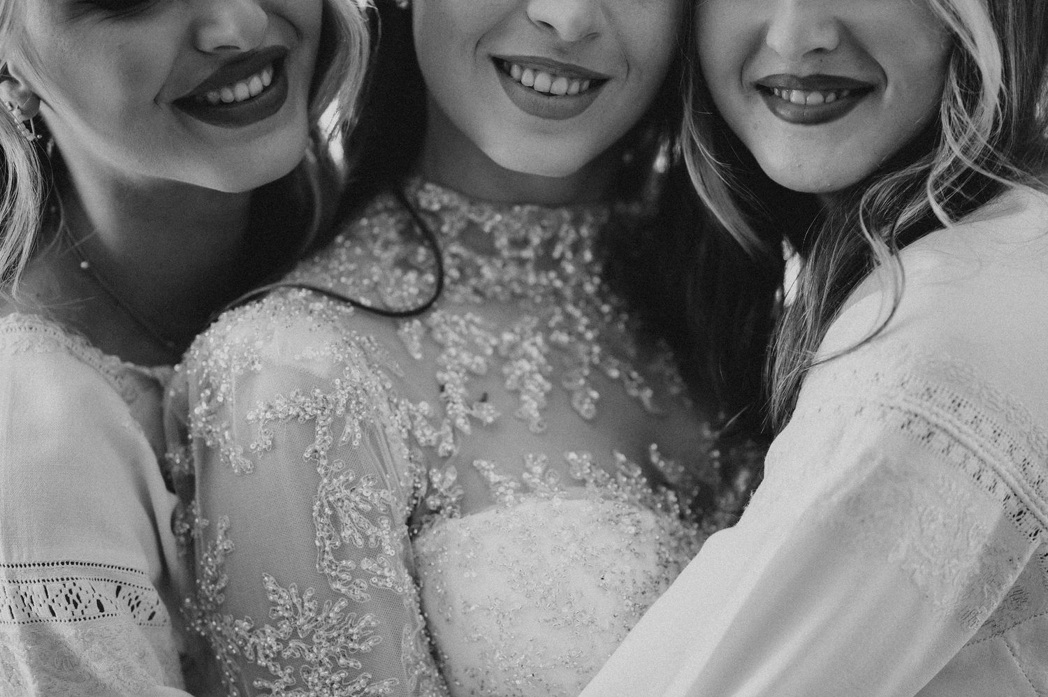 Three smiling women in lace dresses pose together in a black and white bridal photo.