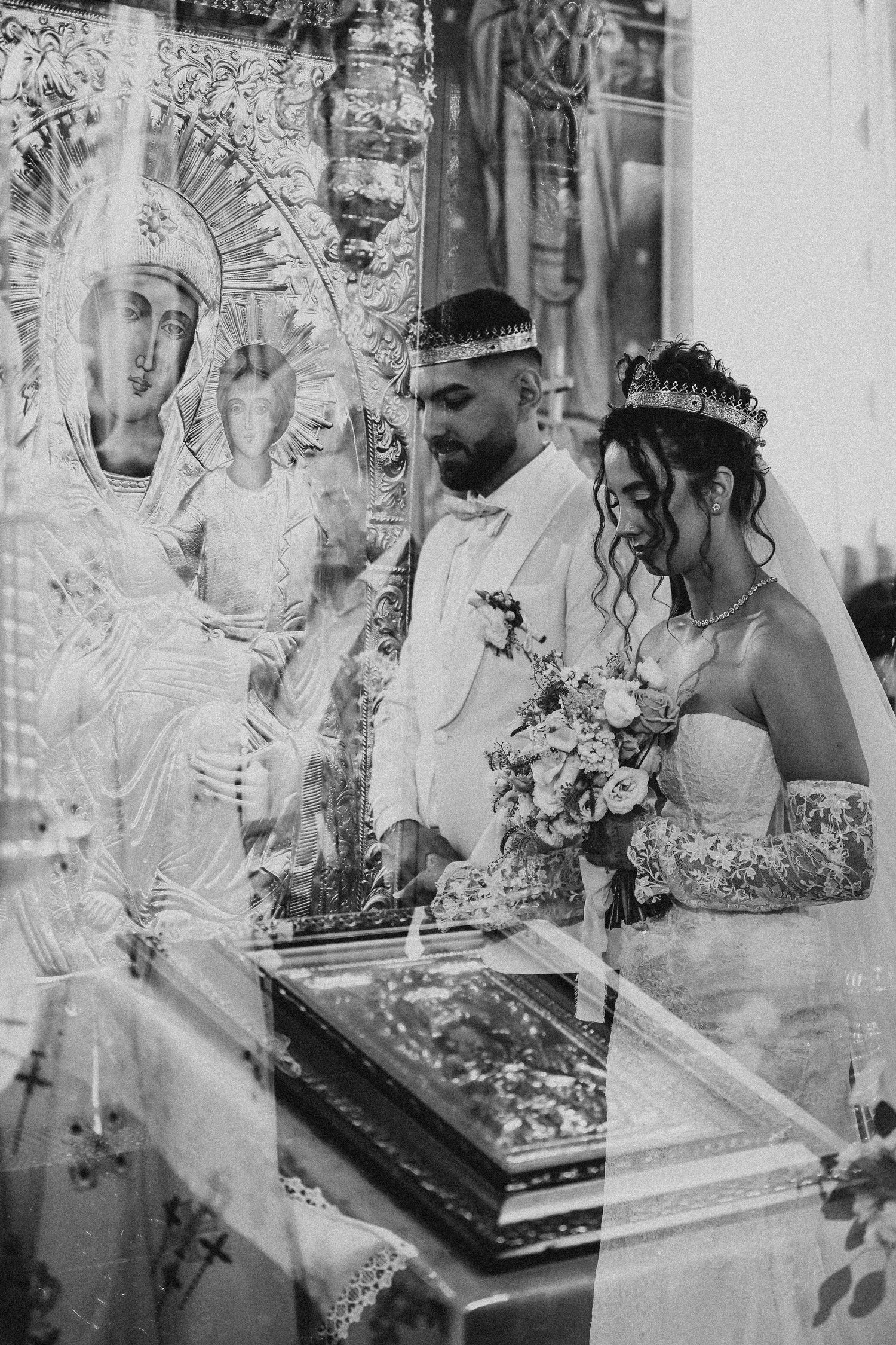 Black and white photo of a bride and groom during an Orthodox Christian wedding ceremony before ornate religious icons.