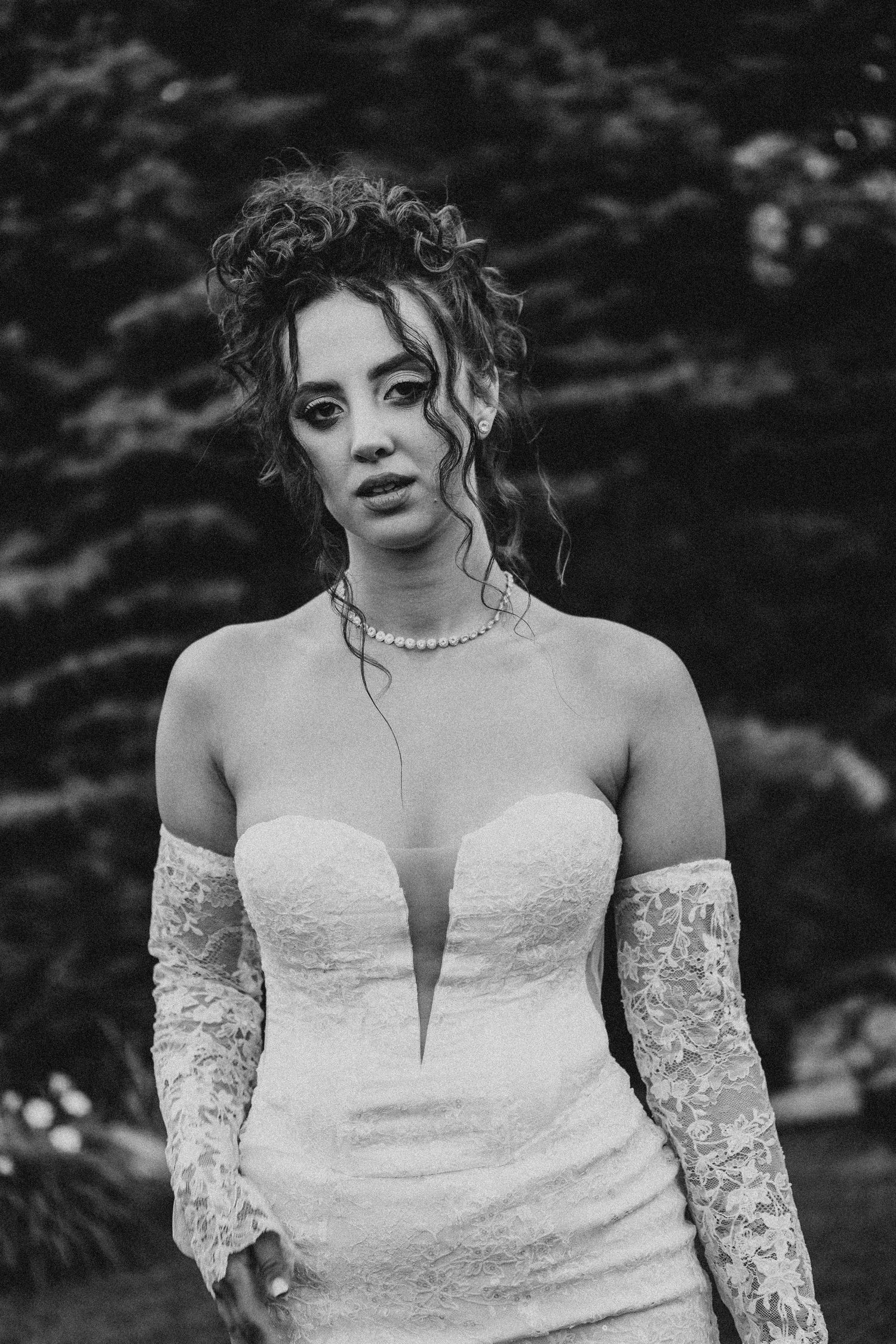 Black and white portrait of a bride in strapless lace wedding gown with long gloves and pearl necklace outdoors.