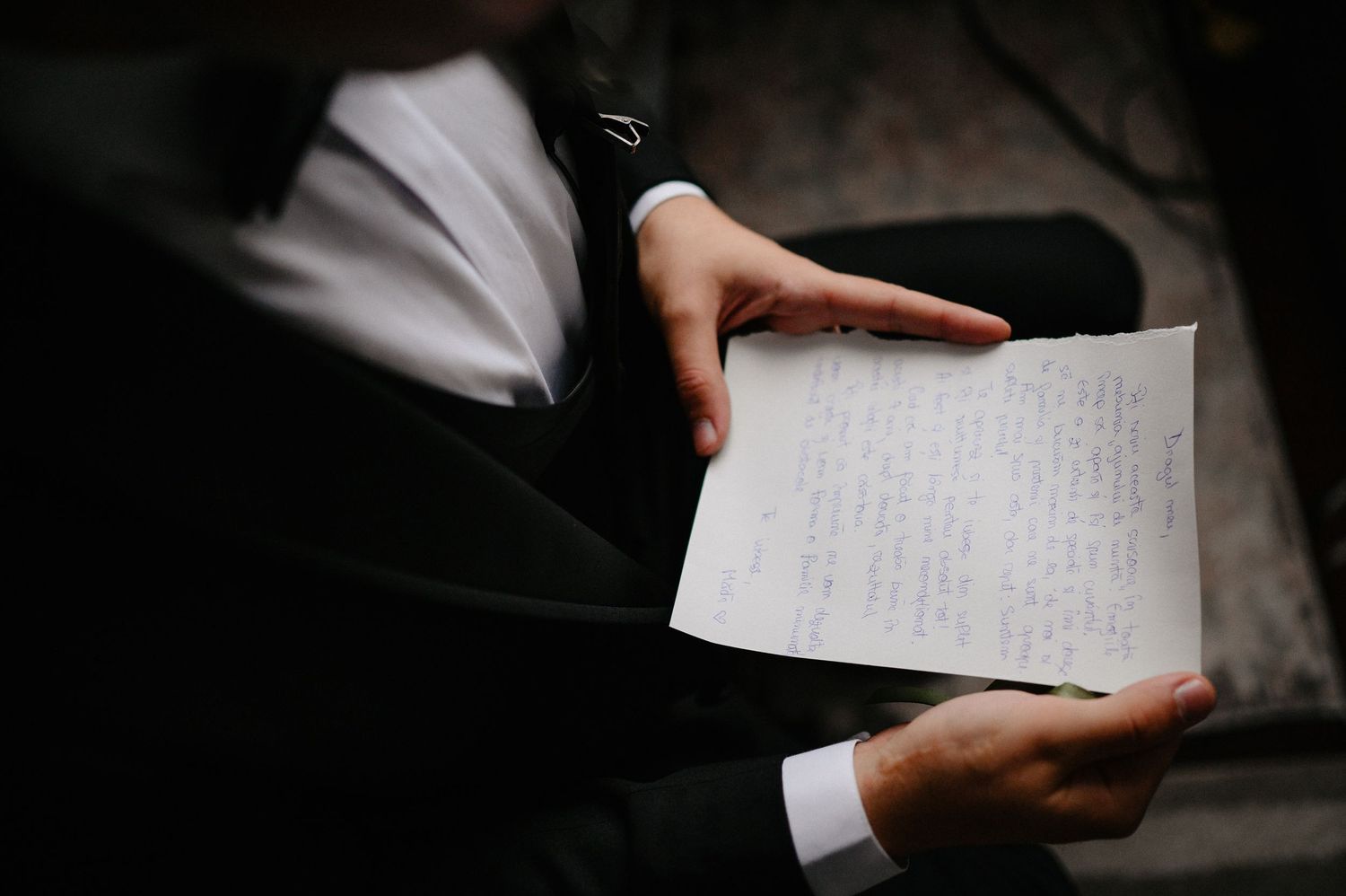 Person in black suit holding handwritten letter, close-up shot of hands reading personal correspondence.