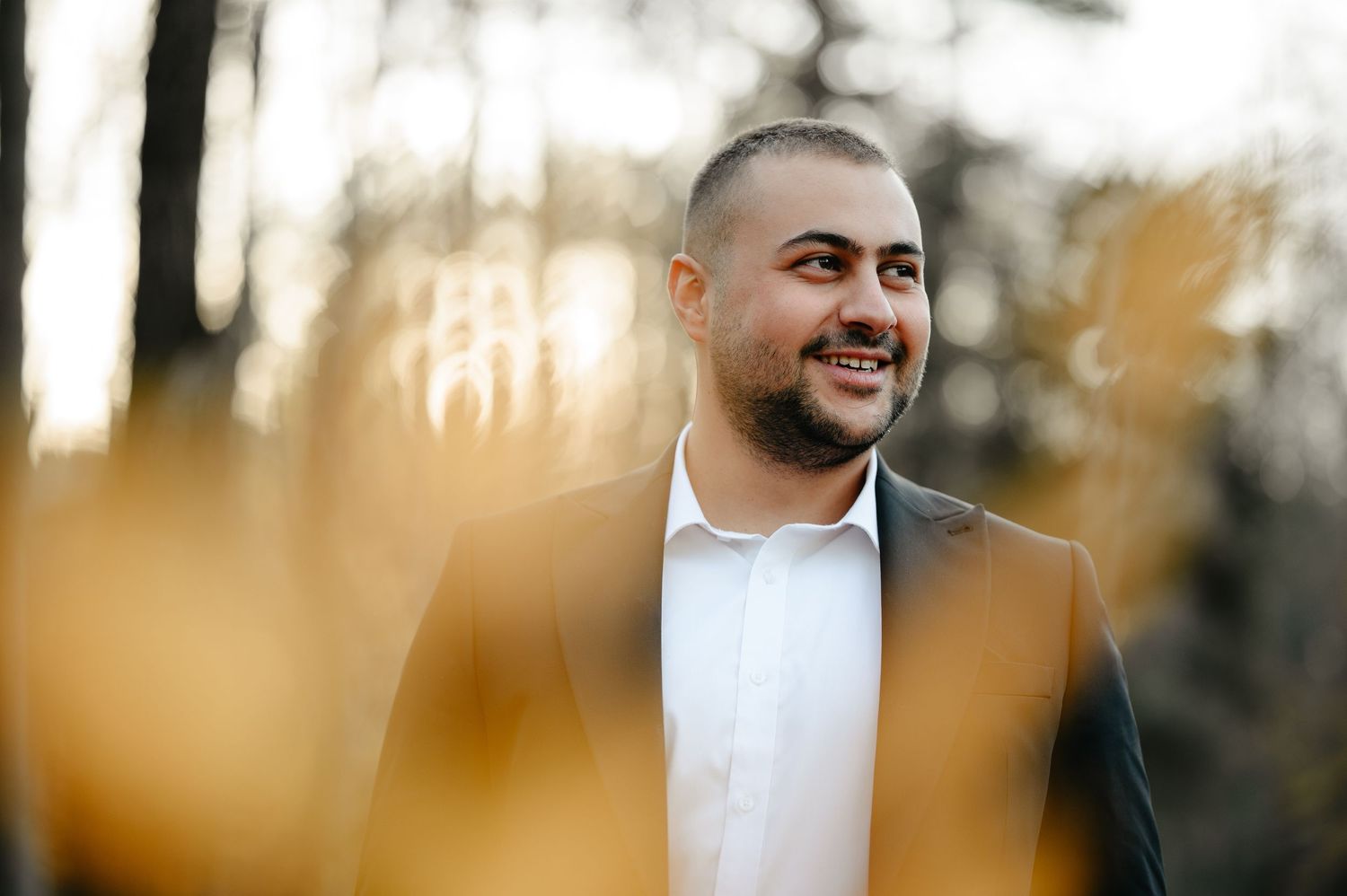 Smiling man in a suit jacket outdoors, with soft bokeh golden foliage background, professional portrait photo.