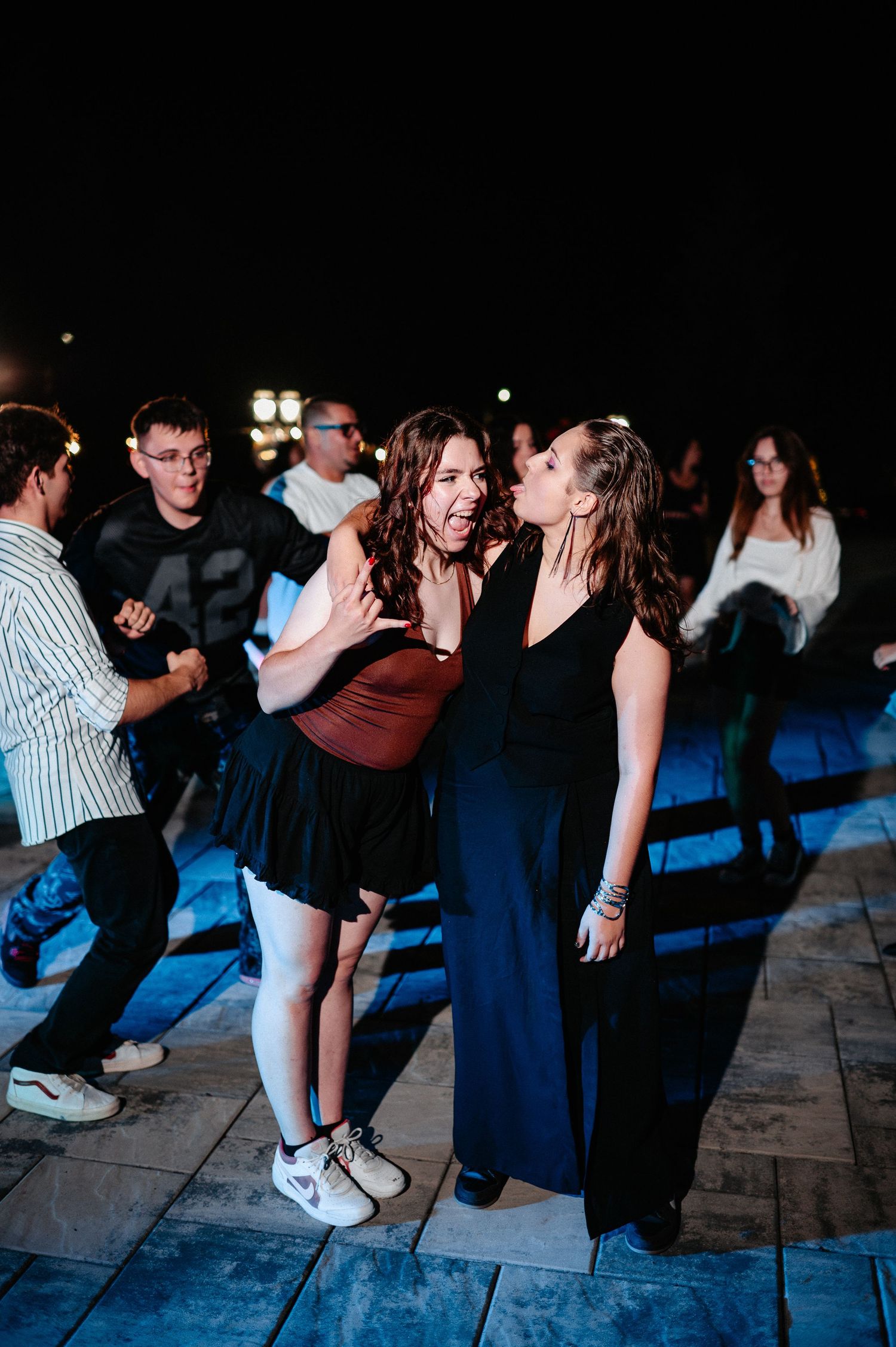 Two women dancing closely together at outdoor night party with crowd of people in background.