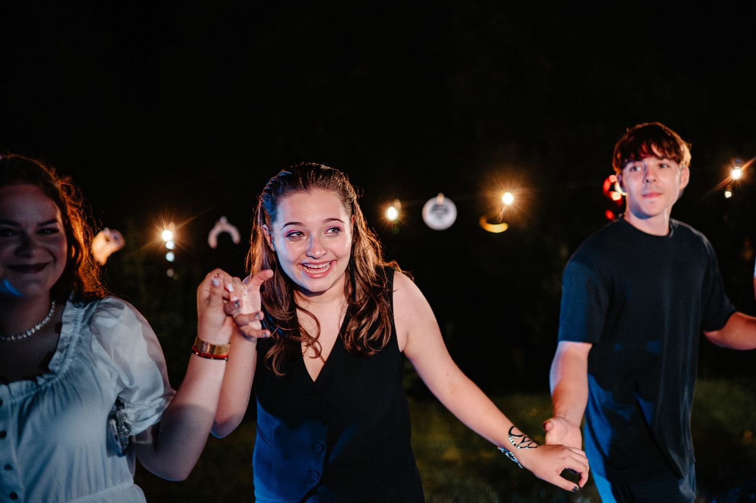 A smiling young woman dances and points at an outdoor nighttime birthday celebration.