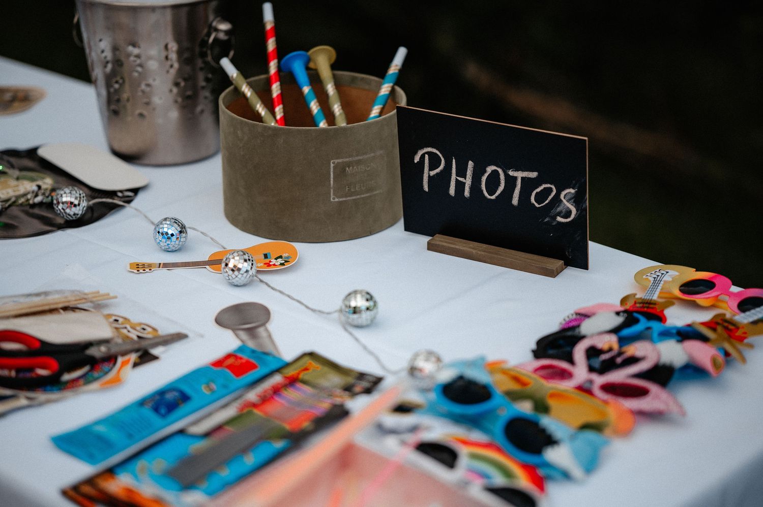 Photo booth props table with chalkboard sign, colorful accessories, and decorative items for party guests.