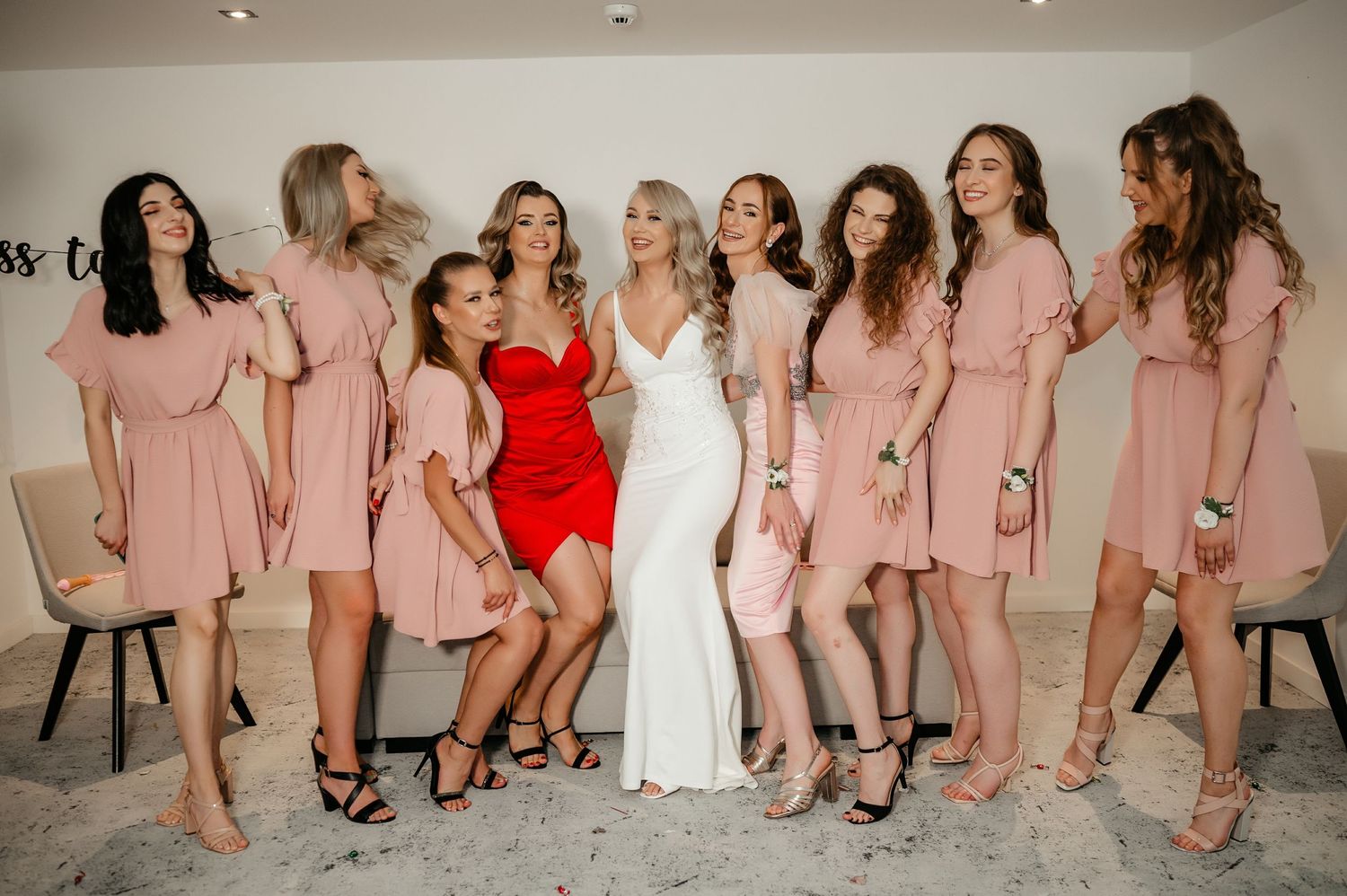 Bride in white gown posing with bridesmaids wearing matching pink dresses in bright room.