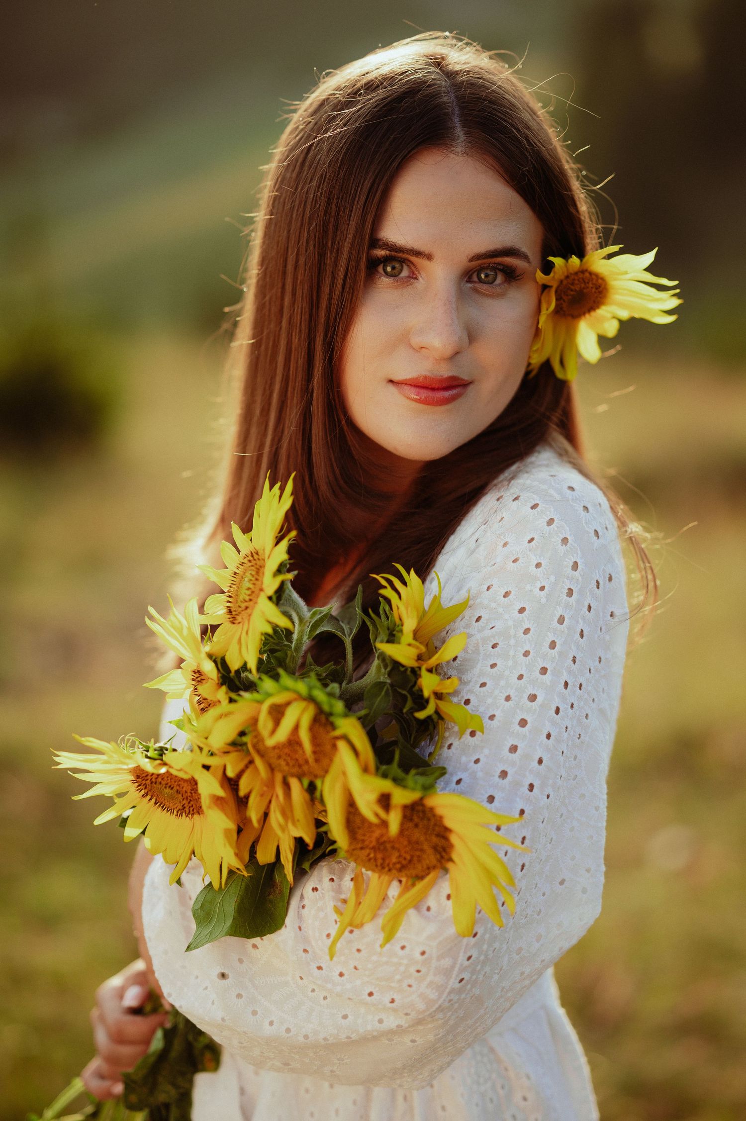 Beautiful brunette woman in white lace dress holding sunflowers in golden natural light.
