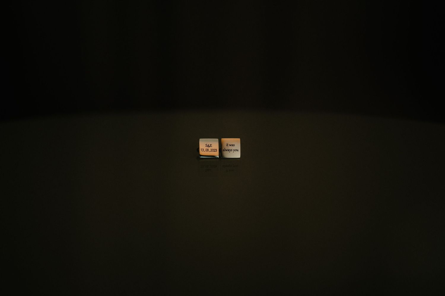 Two small square cufflinks illuminated against a dark background.