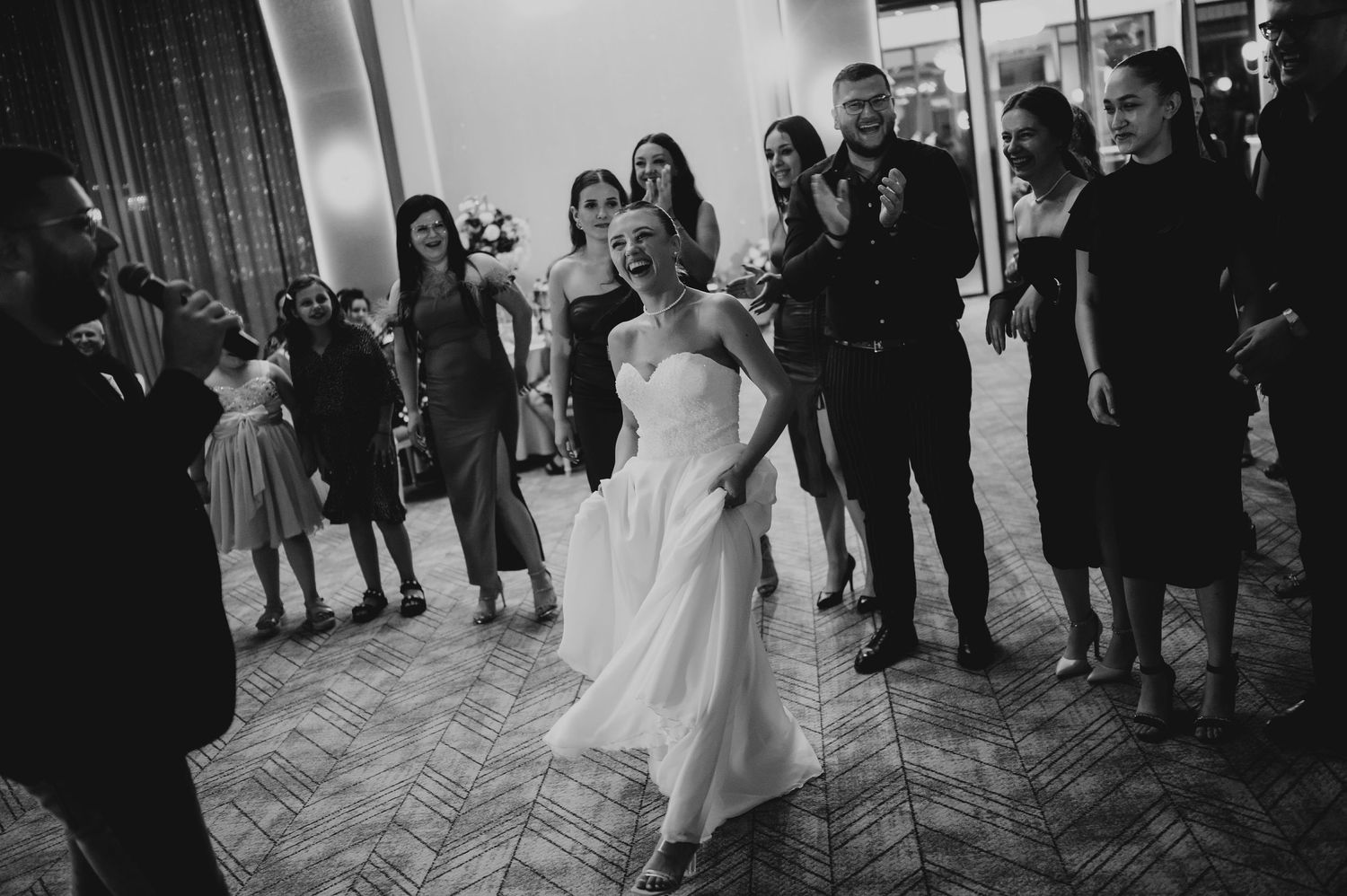 Bride dancing joyfully on wedding reception dance floor in black and white photo with guests watching.