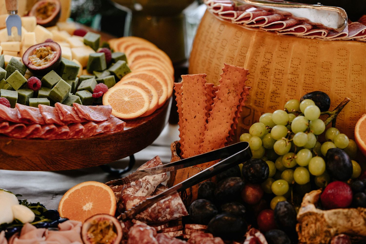 Luxurious grazing table with a giant Parmigiano Reggiano wheel, grapes, cured meats, and colorful antipasti.