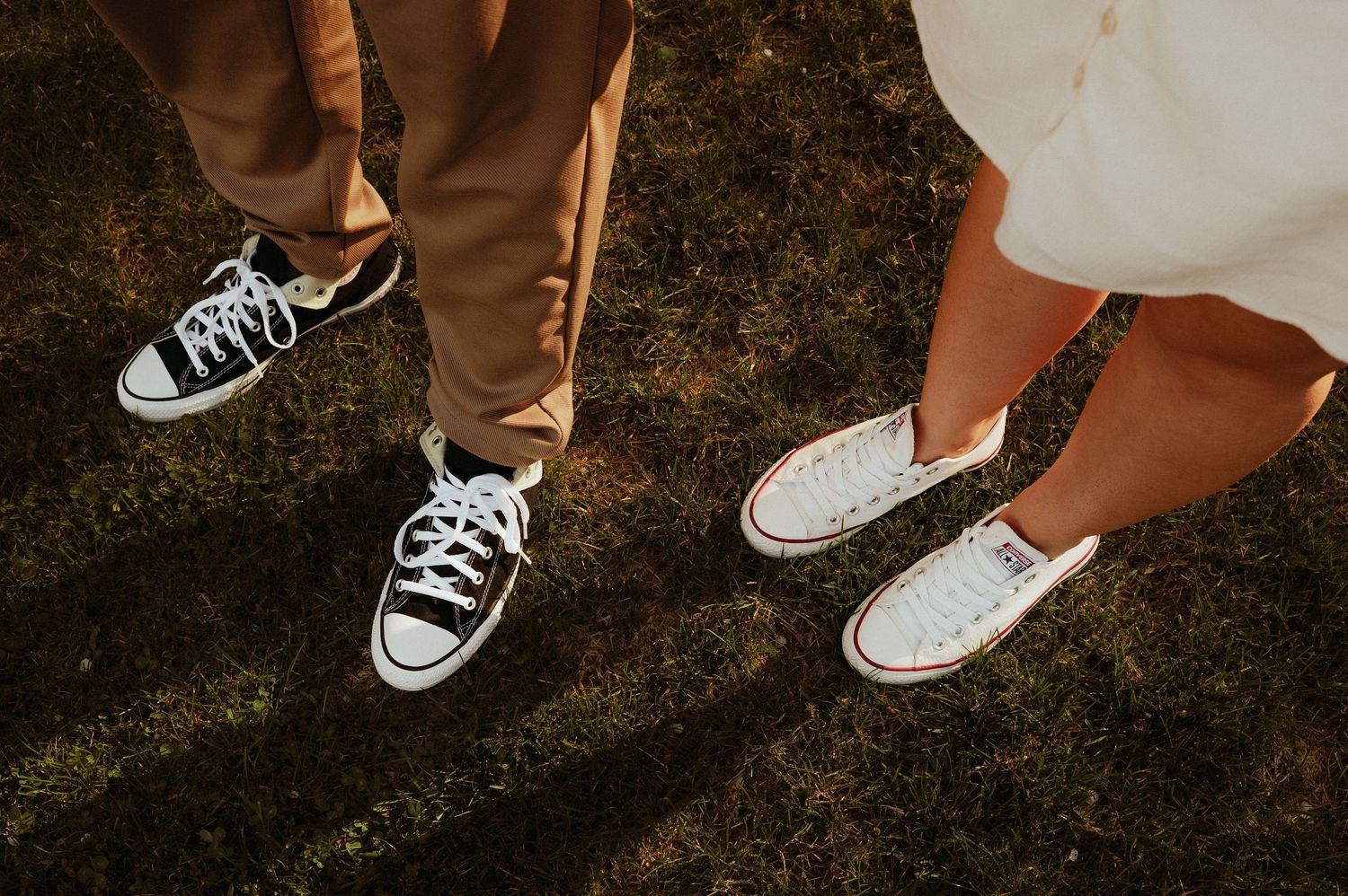 Close-up of couple wearing matching Converse sneakers standing on green grass during outdoor photo session.