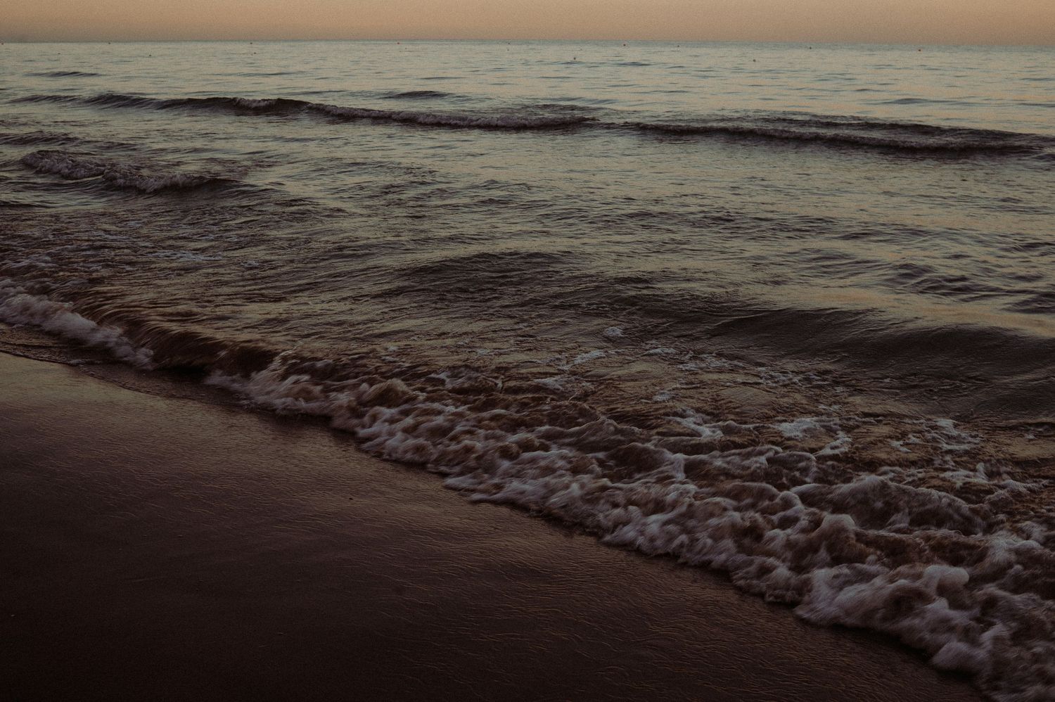 Gentle ocean waves washing onto a sandy beach during a peaceful sunset evening.
