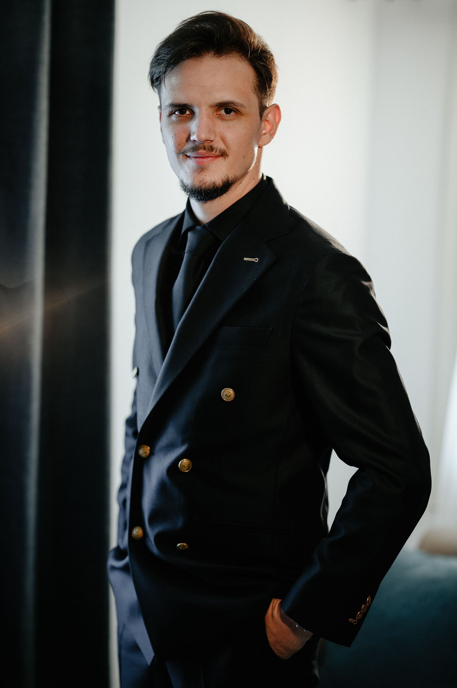 Confident groom in a black double-breasted suit smiling with hand in pocket.