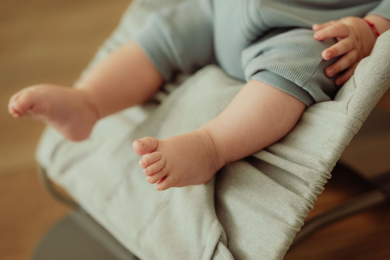 Close-up of chubby baby feet and legs in a light blue outfit resting in a bouncer.