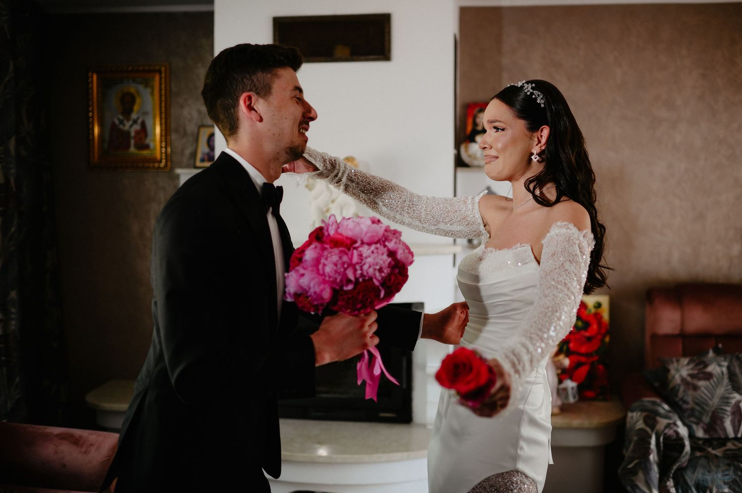 Bride tenderly touches grooms face during first look while holding pink and red bouquets.