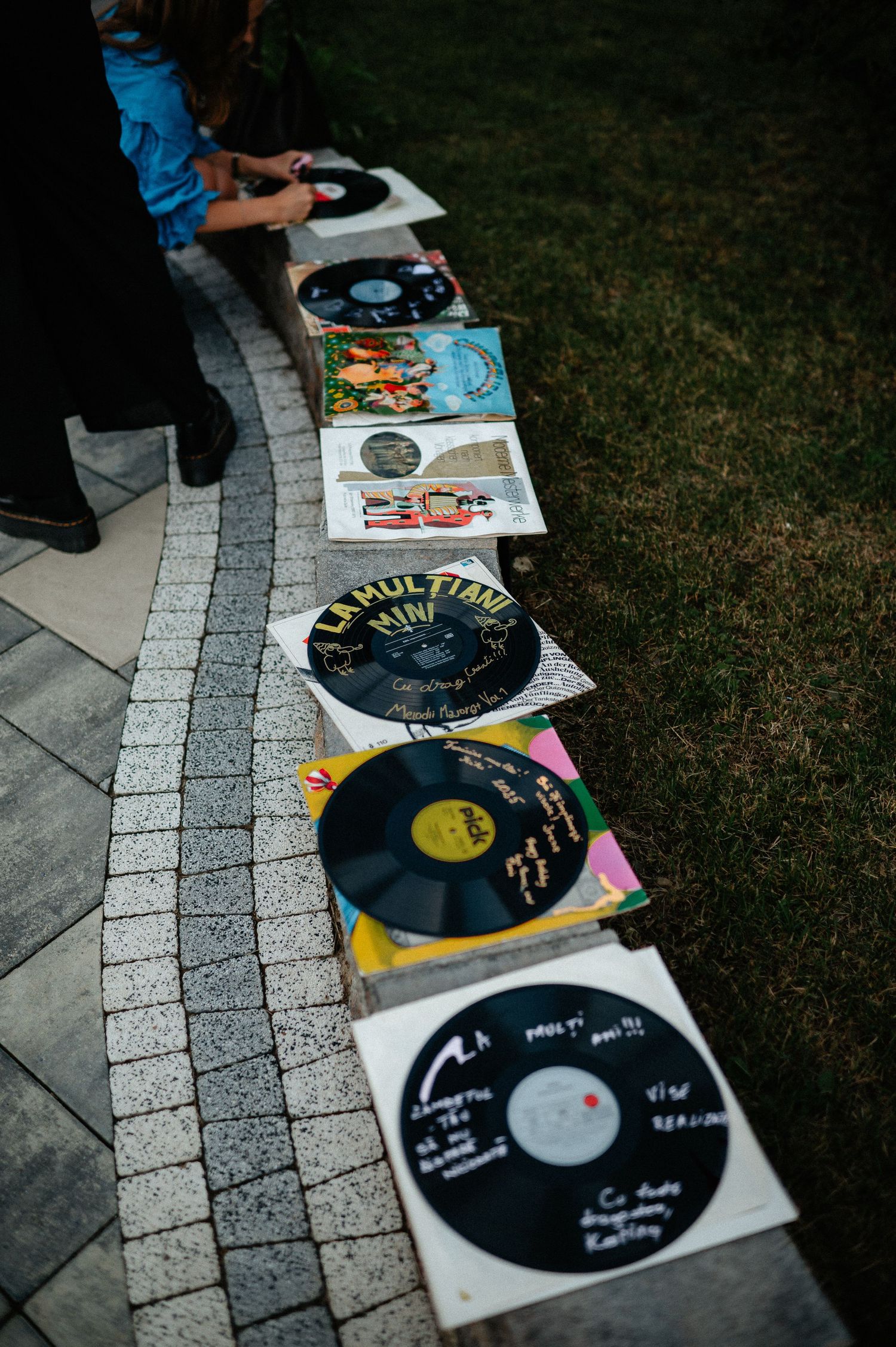 Vinyl records with handwritten messages displayed on a stone pathway at an outdoor celebration.