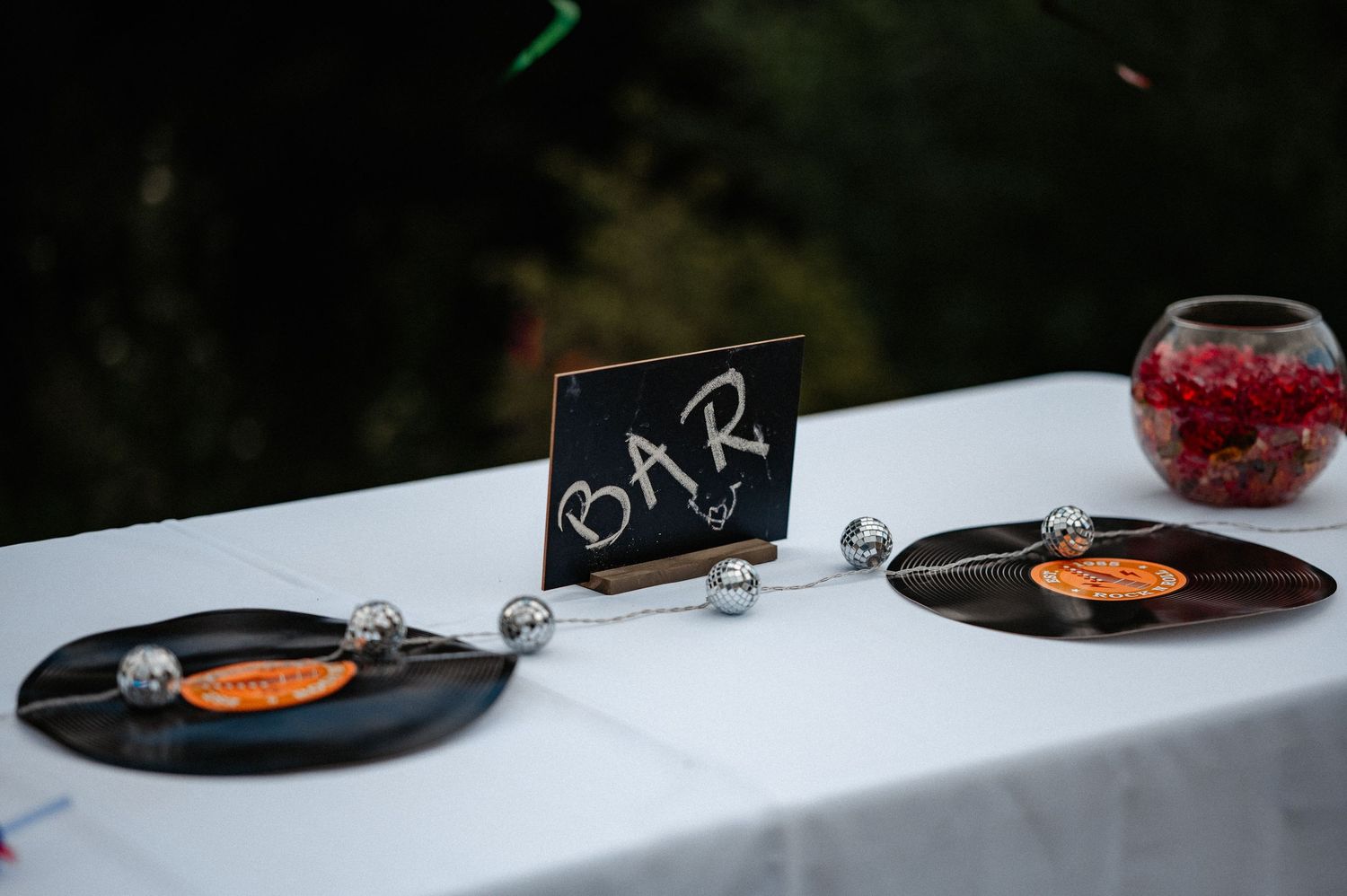 Bar table decorated with vinyl records, silver disco balls, and chalkboard sign at music party.
