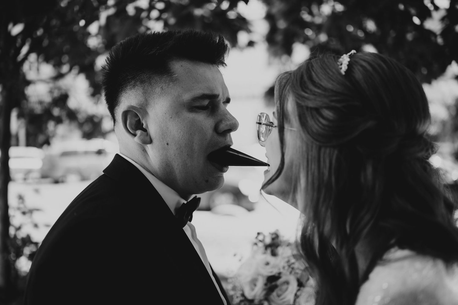Black and white photo of bride and groom sharing a chocolate stick kiss at their wedding.