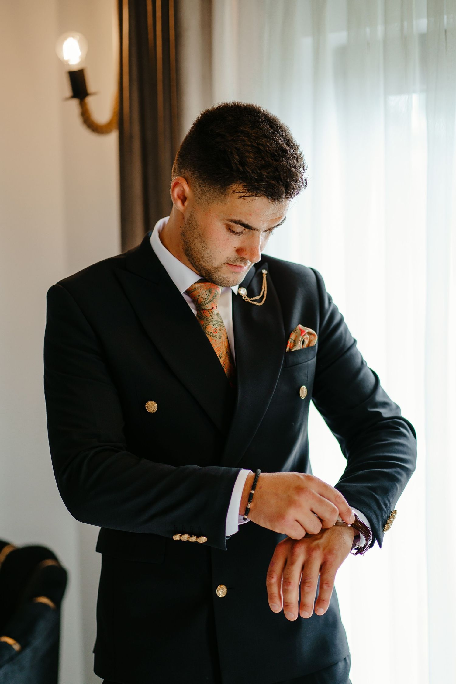 Groom in black double-breasted suit adjusting cufflinks before wedding ceremony.