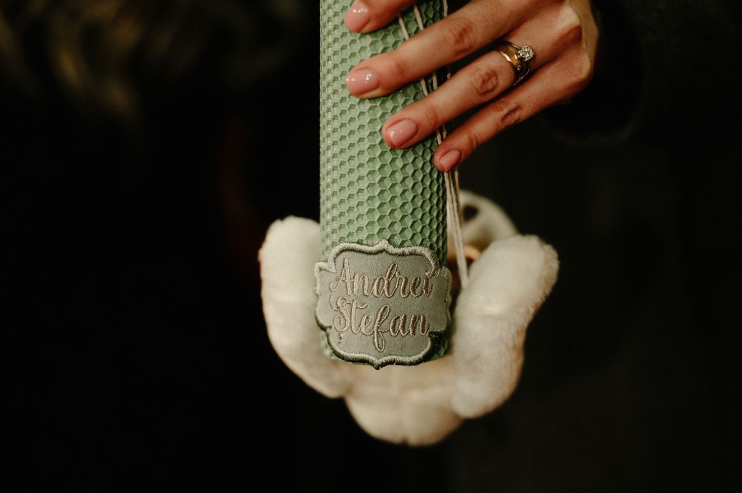 Hand with ring holding a green textured candle with decorative silver label.