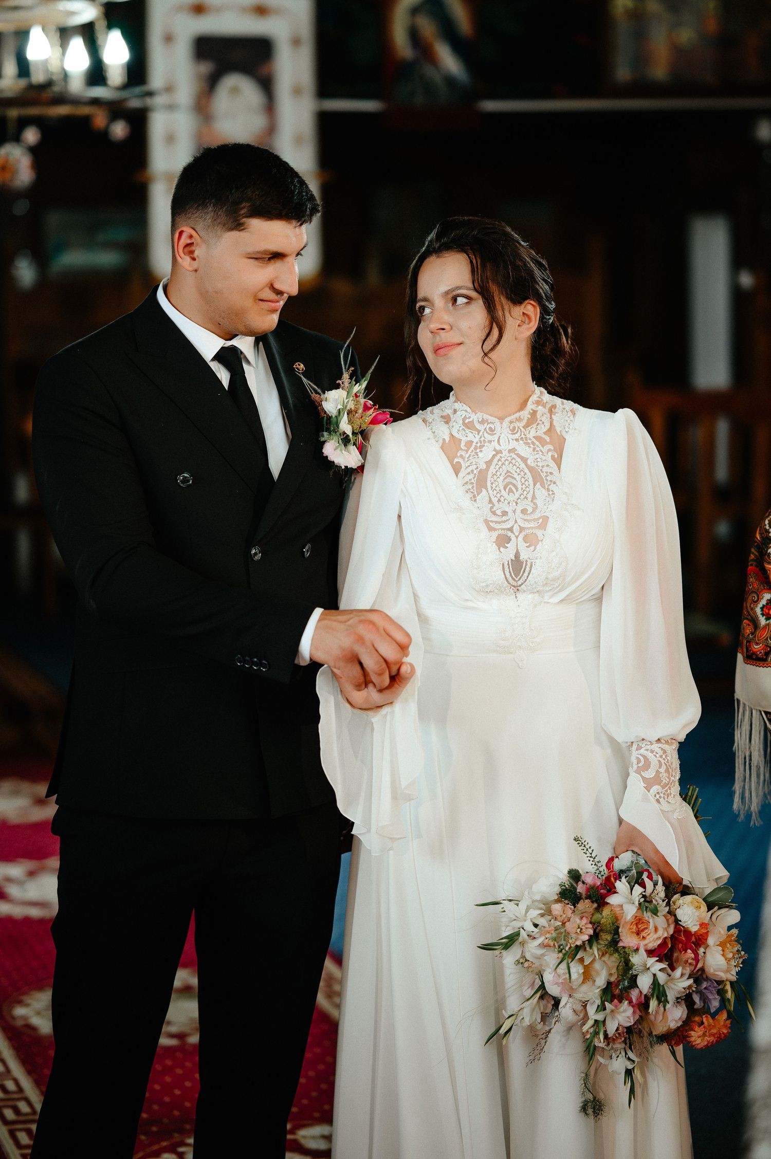 Bride and groom exchange rings during Orthodox church wedding ceremony, bride holding vibrant floral bouquet.