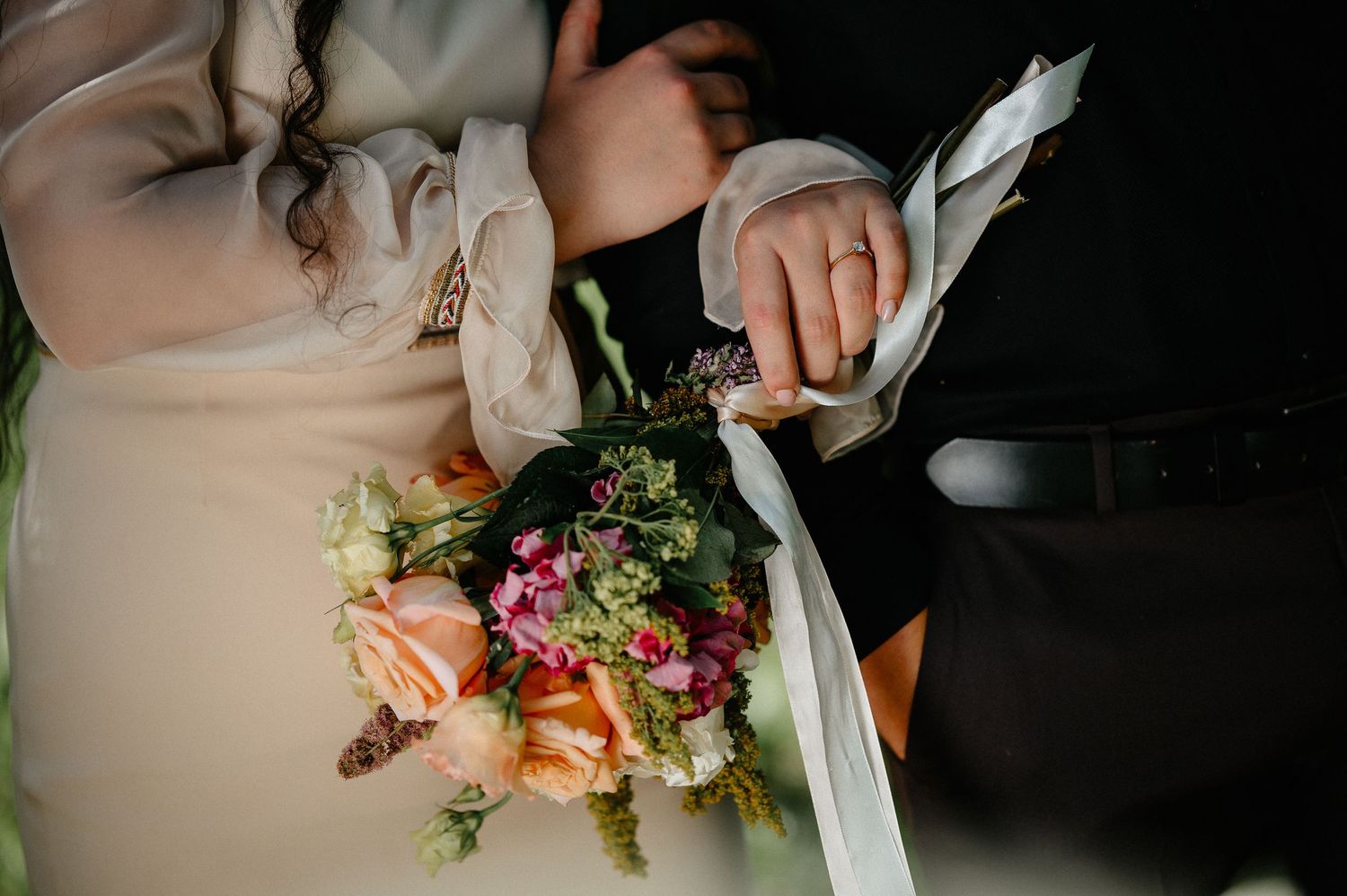 Bride and groom holding a colorful wedding bouquet with ribbon details.