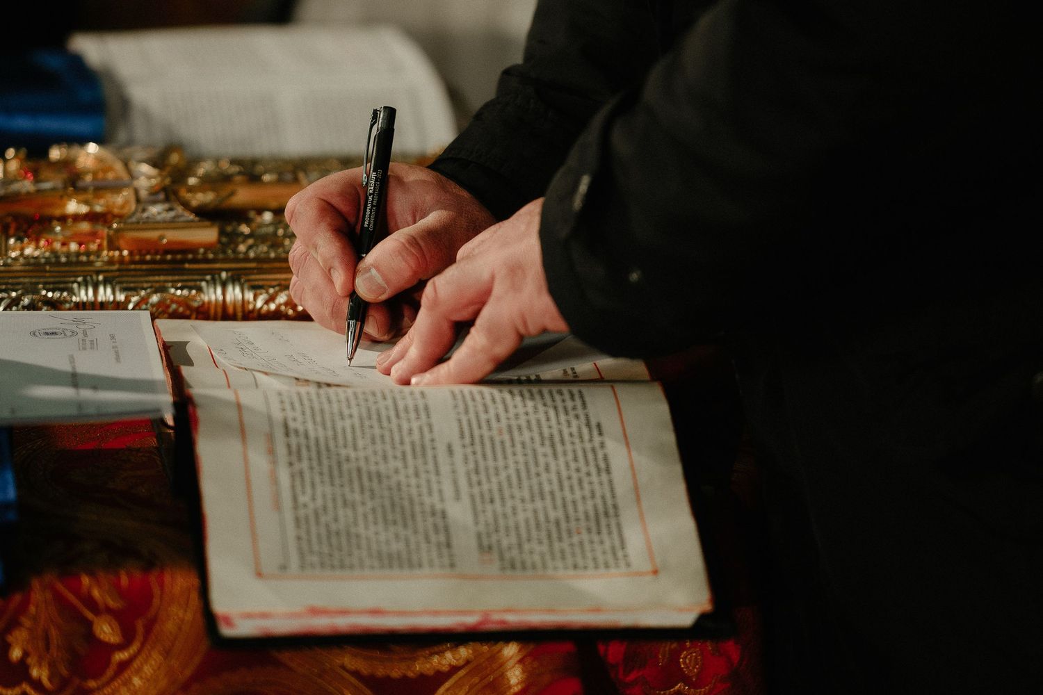 Close-up of hands signing an open religious text book with a black pen.
