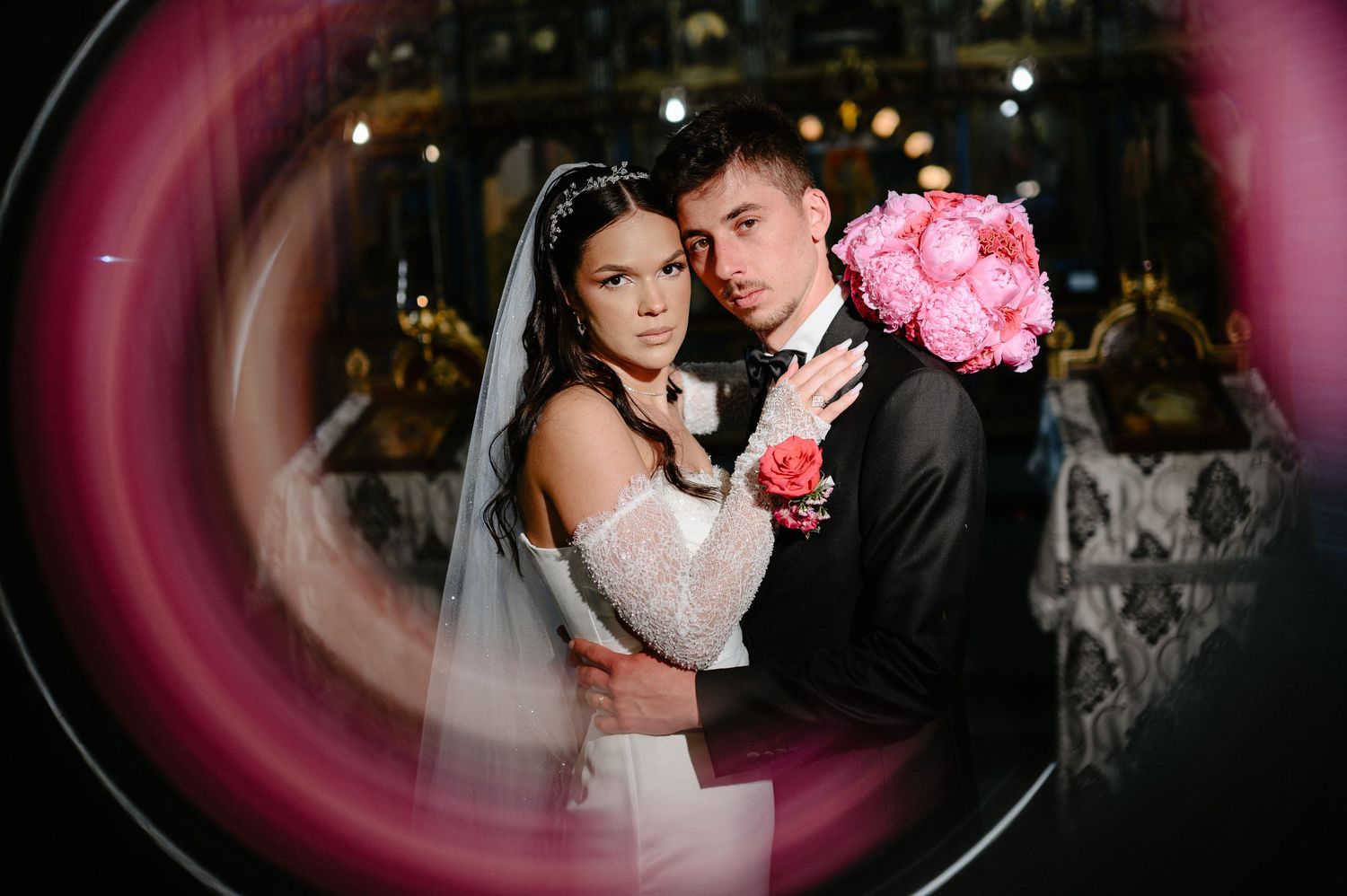 Creative circular framed portrait of bride and groom embracing inside an ornate Orthodox church.