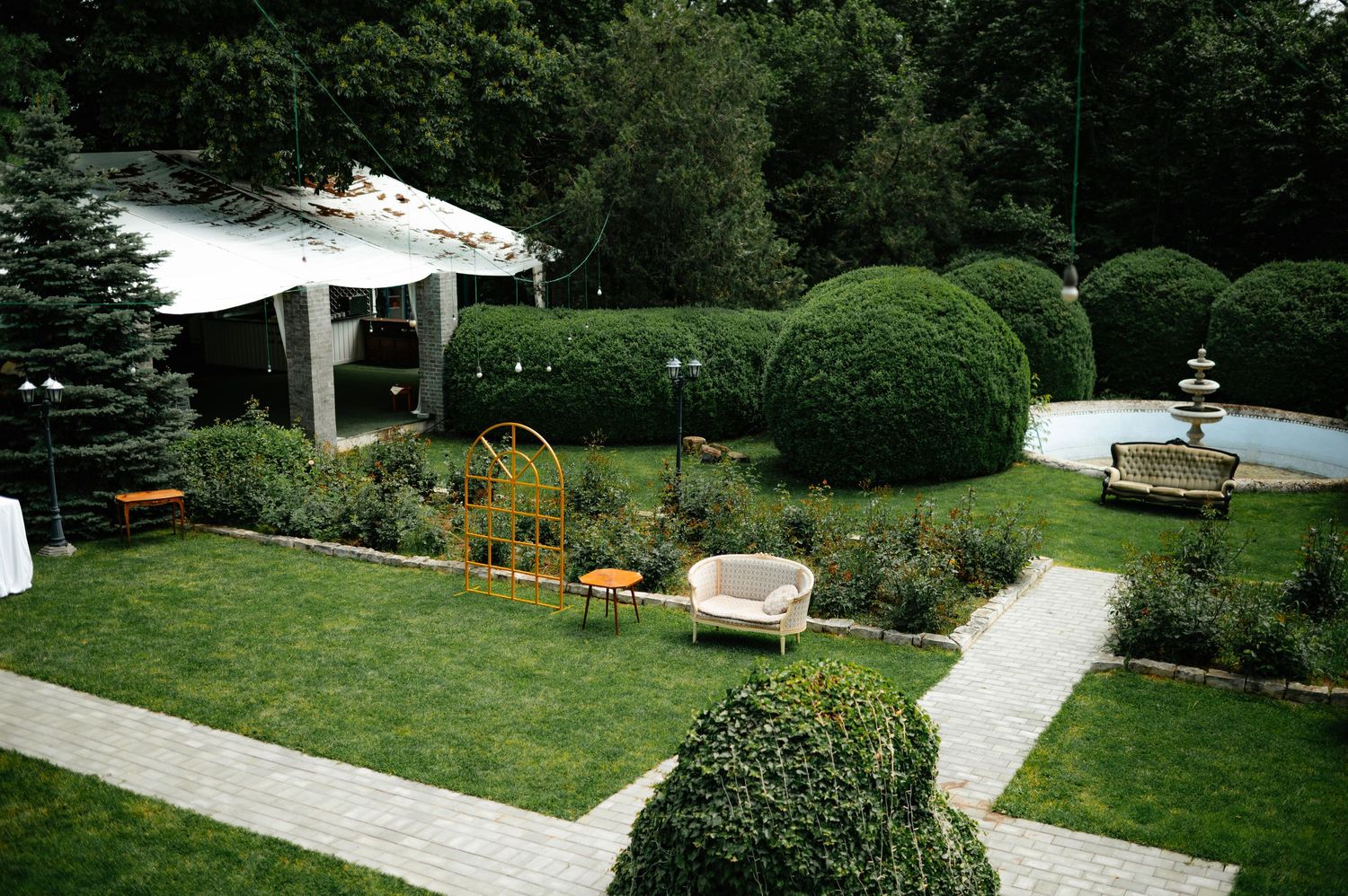 Manicured garden with topiary bushes, fountain, and white tent for outdoor wedding venue.