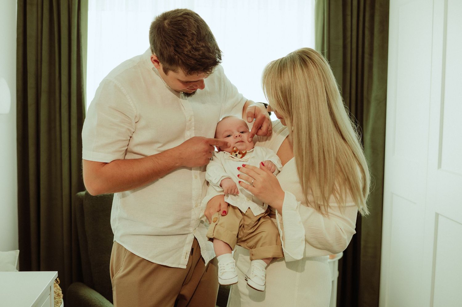 Young parents in neutral tones admiring their newborn baby together in a bright, cozy room.