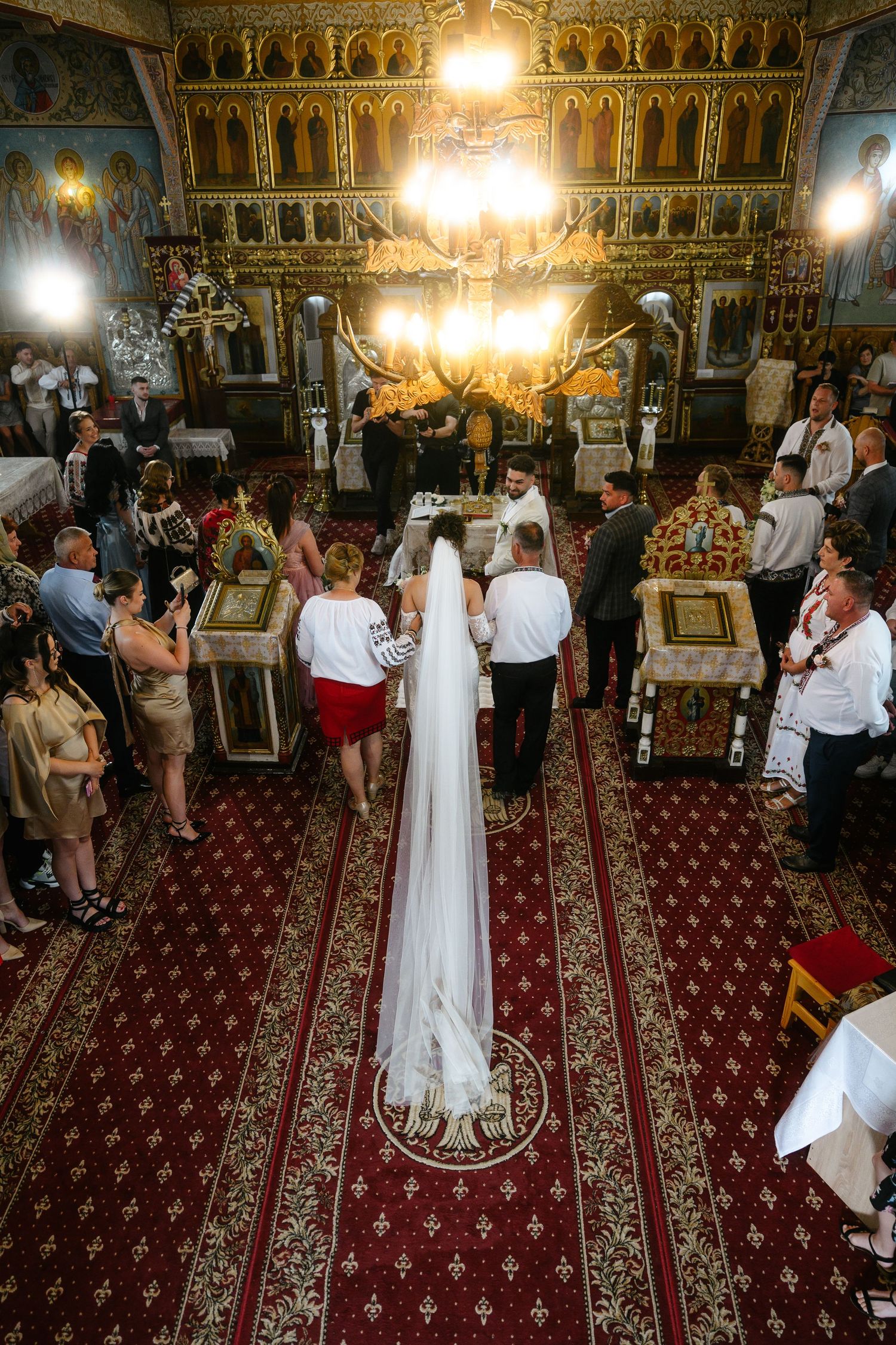 Orthodox church wedding ceremony with bride in white veil and groom standing before altar surrounded by guests.