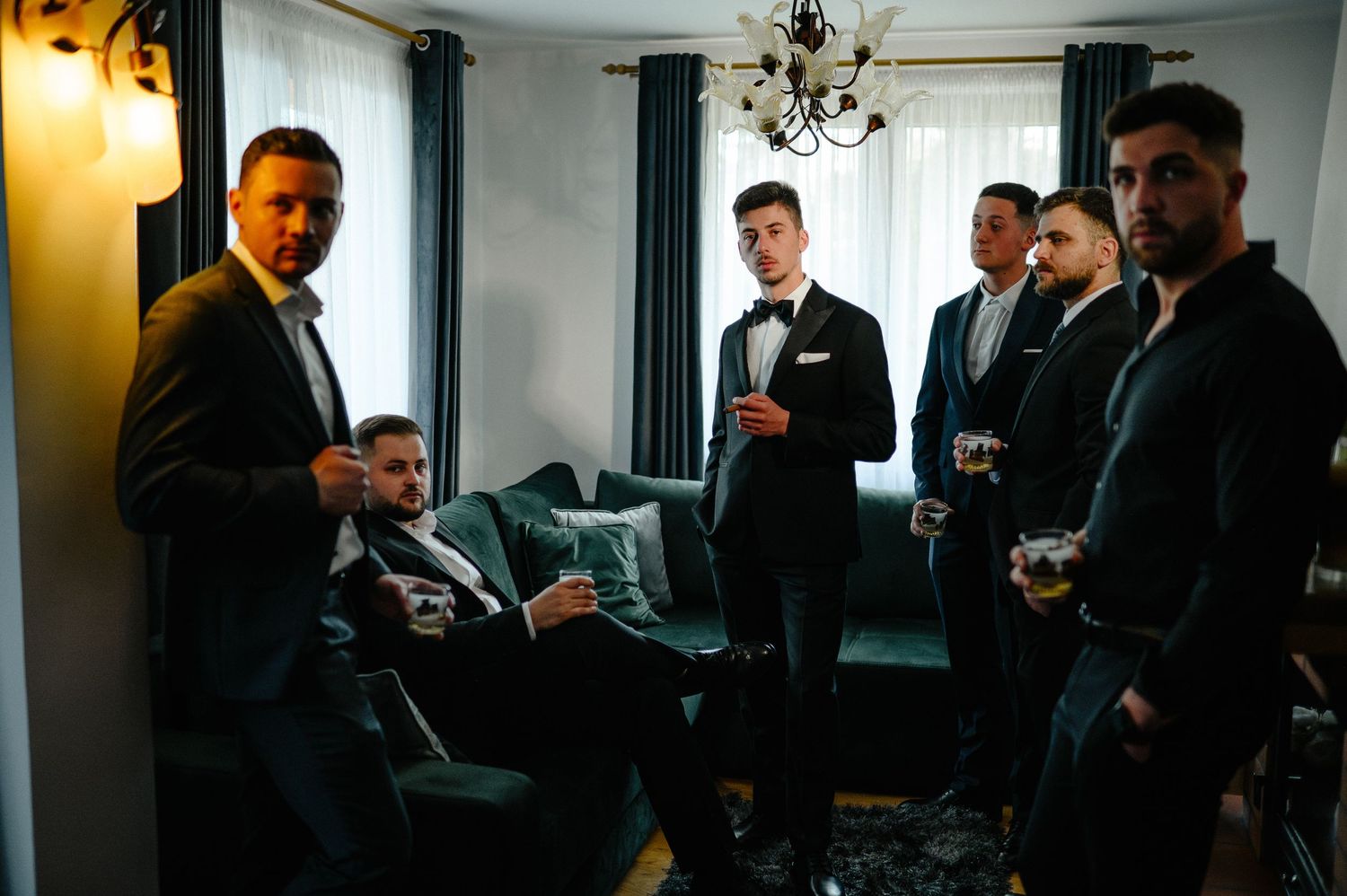 Groomsmen in dark suits relaxing together in elegant room before wedding.
