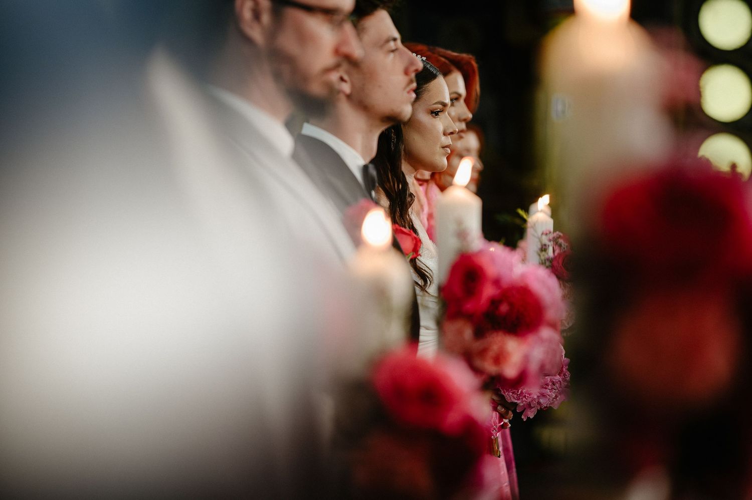 Wedding guests holding candles and pink bouquets during a romantic candlelit church ceremony.