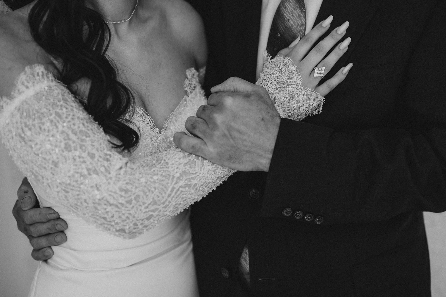 Black and white close-up of bride in lace wedding dress and groom in suit embracing tenderly.