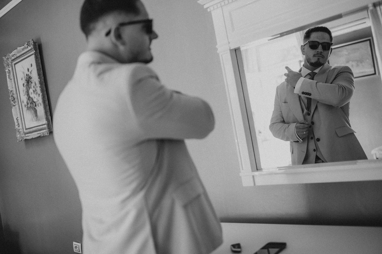 Groom fixing tie while checking reflection in mirror before wedding.