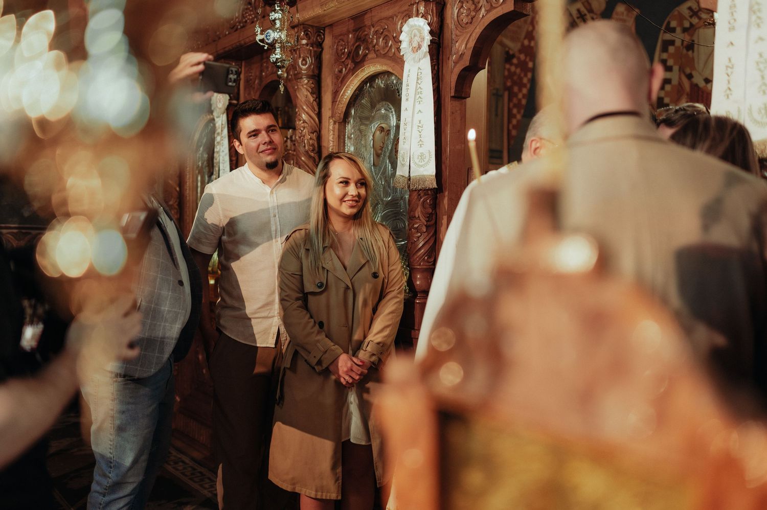 Young couple standing reverently inside an ornate Orthodox church during a baptism service.