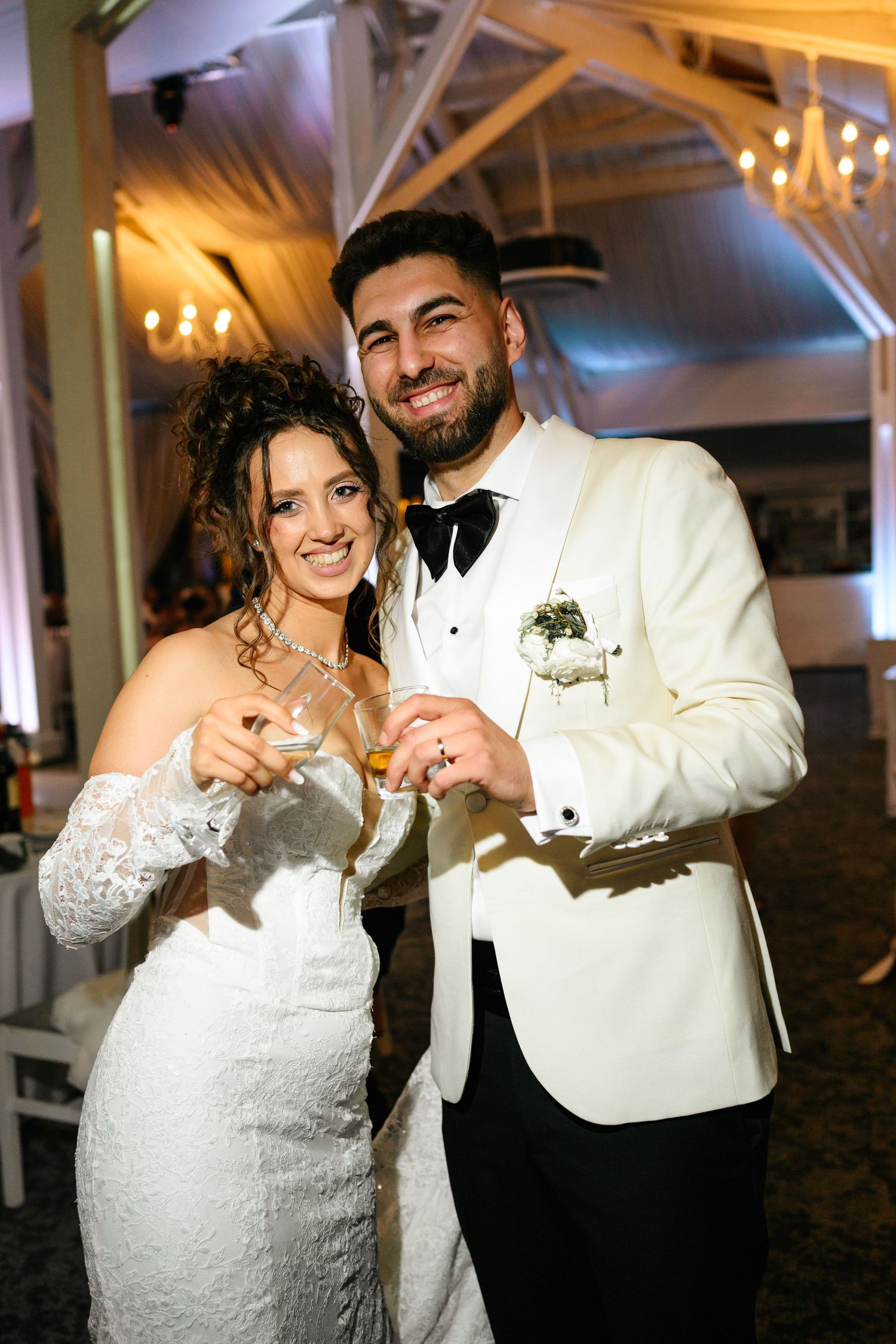 Smiling bride and groom in white tuxedo toasting with champagne glasses at elegant wedding reception.