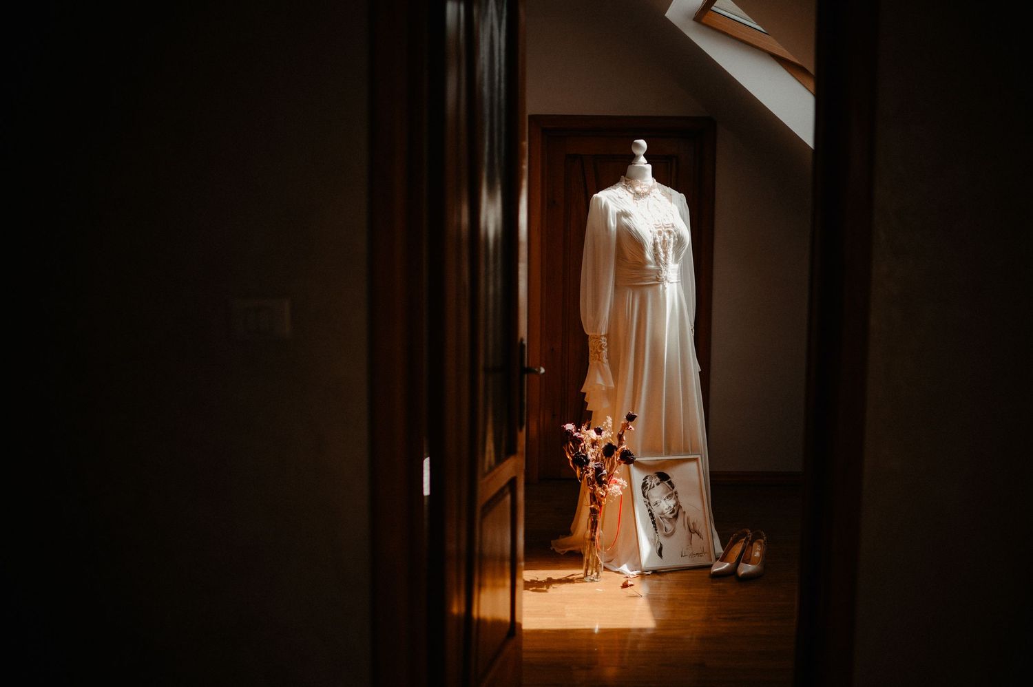 White wedding dress on mannequin displayed in sunlit room with bridal accessories nearby.