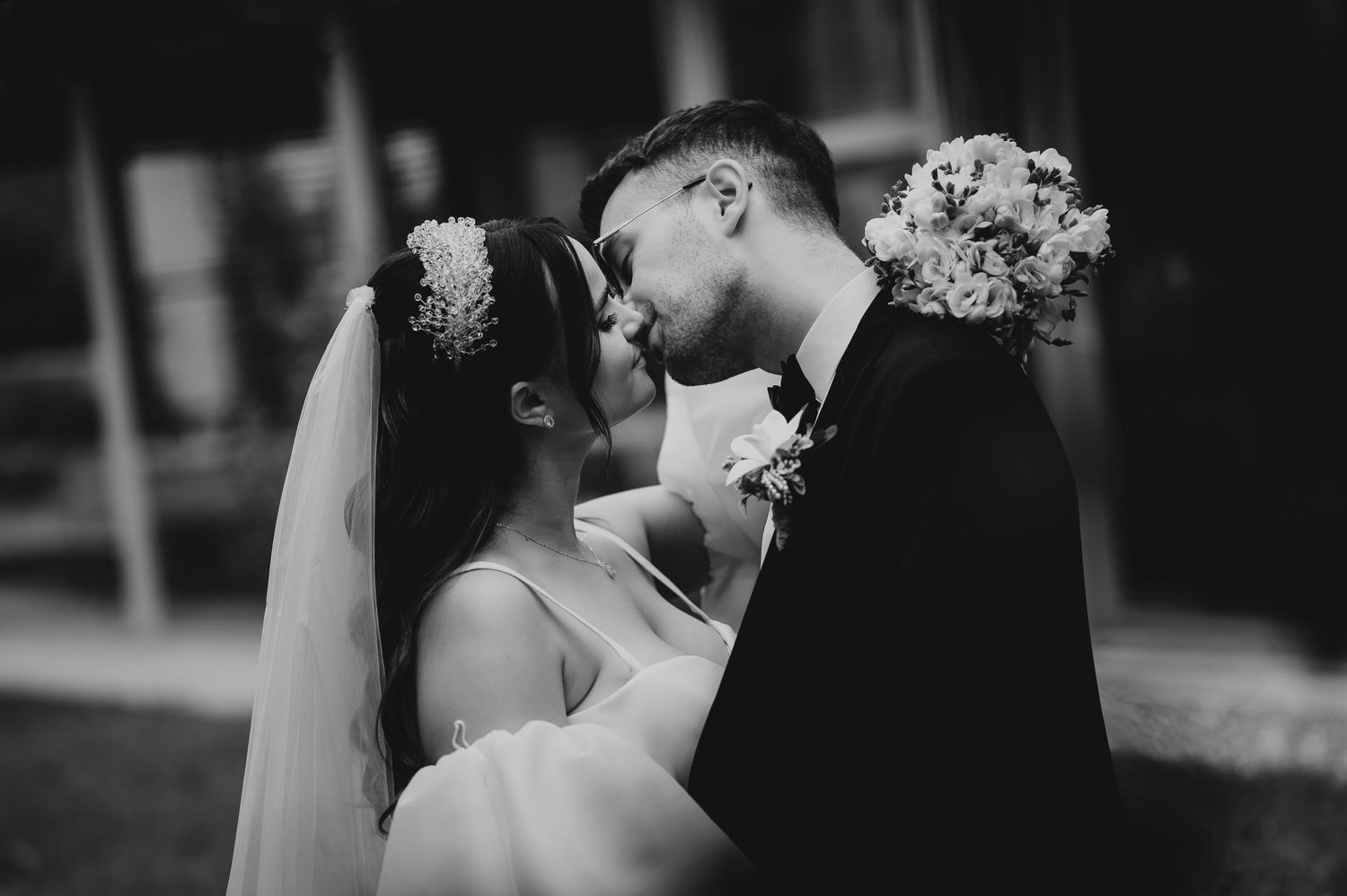 Black and white photo of a bride and groom sharing a romantic kiss on their wedding day.