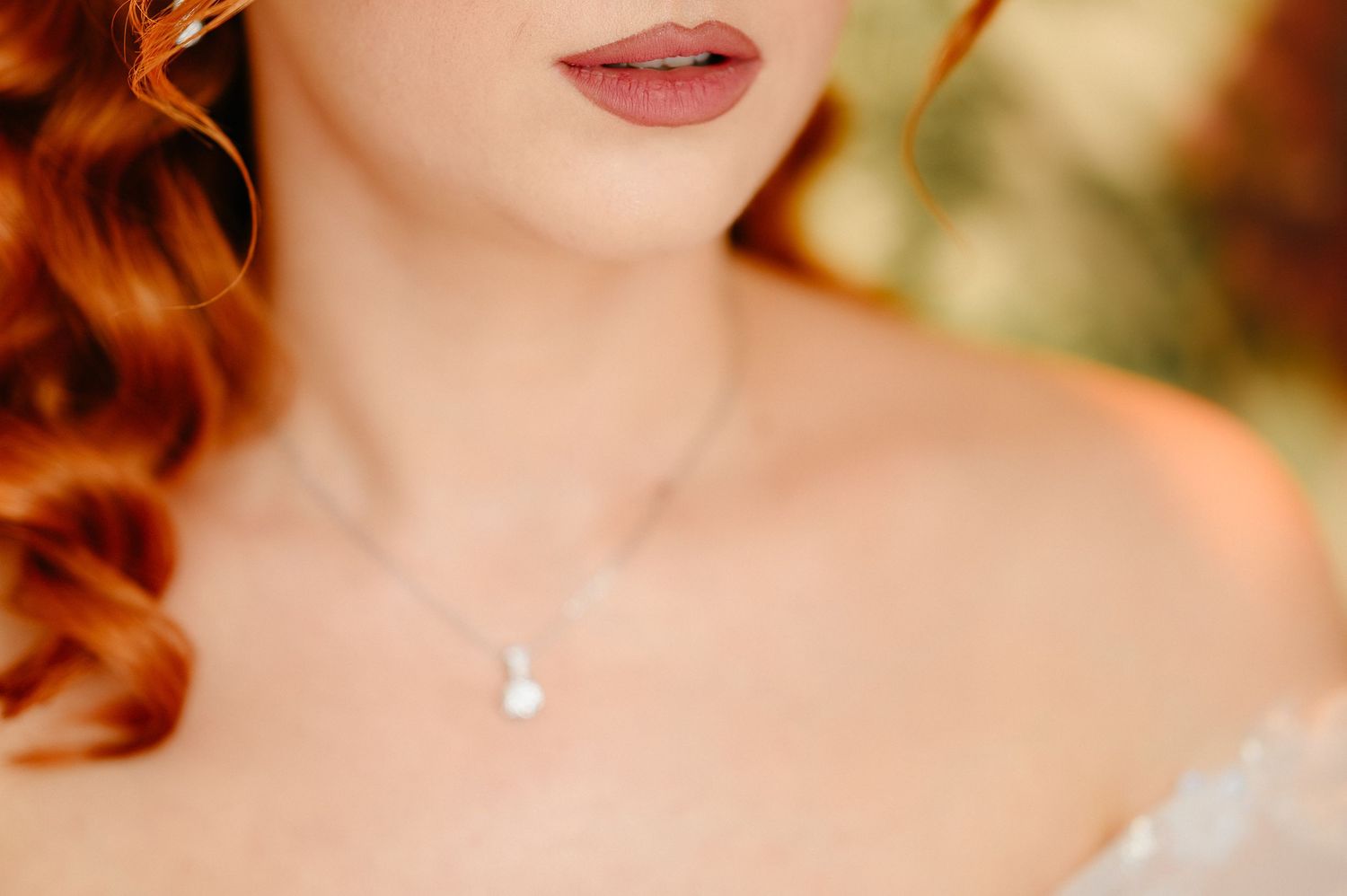 Close-up of a bride wearing a pearl pendant necklace with red curly hair and soft pink lips.