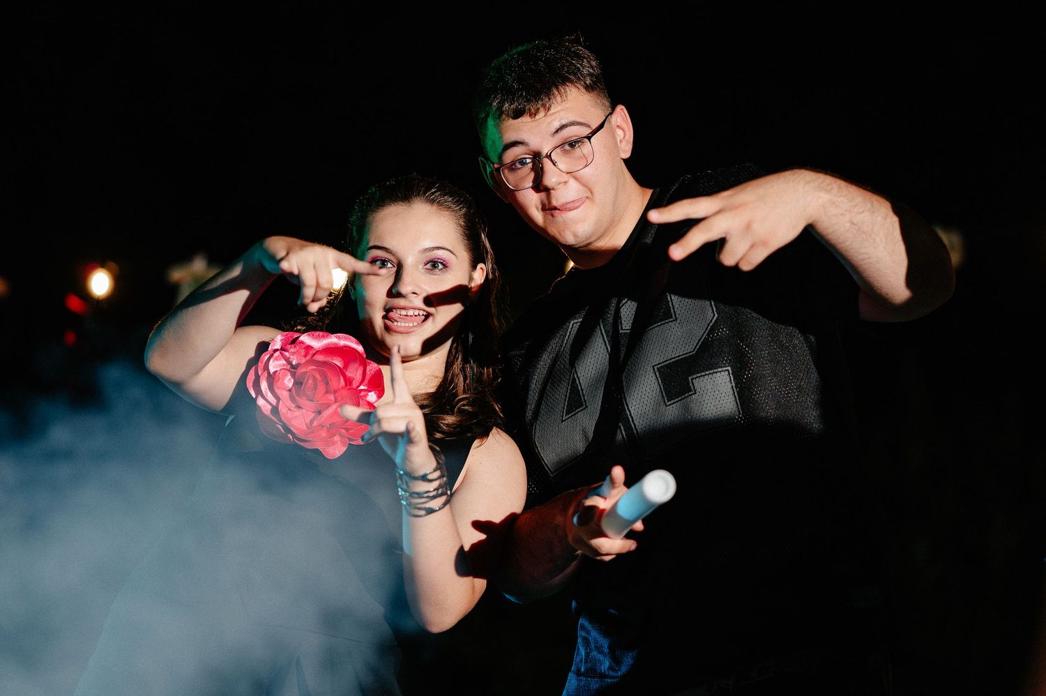 Two friends posing playfully with a rose and smoke effects at a night party.
