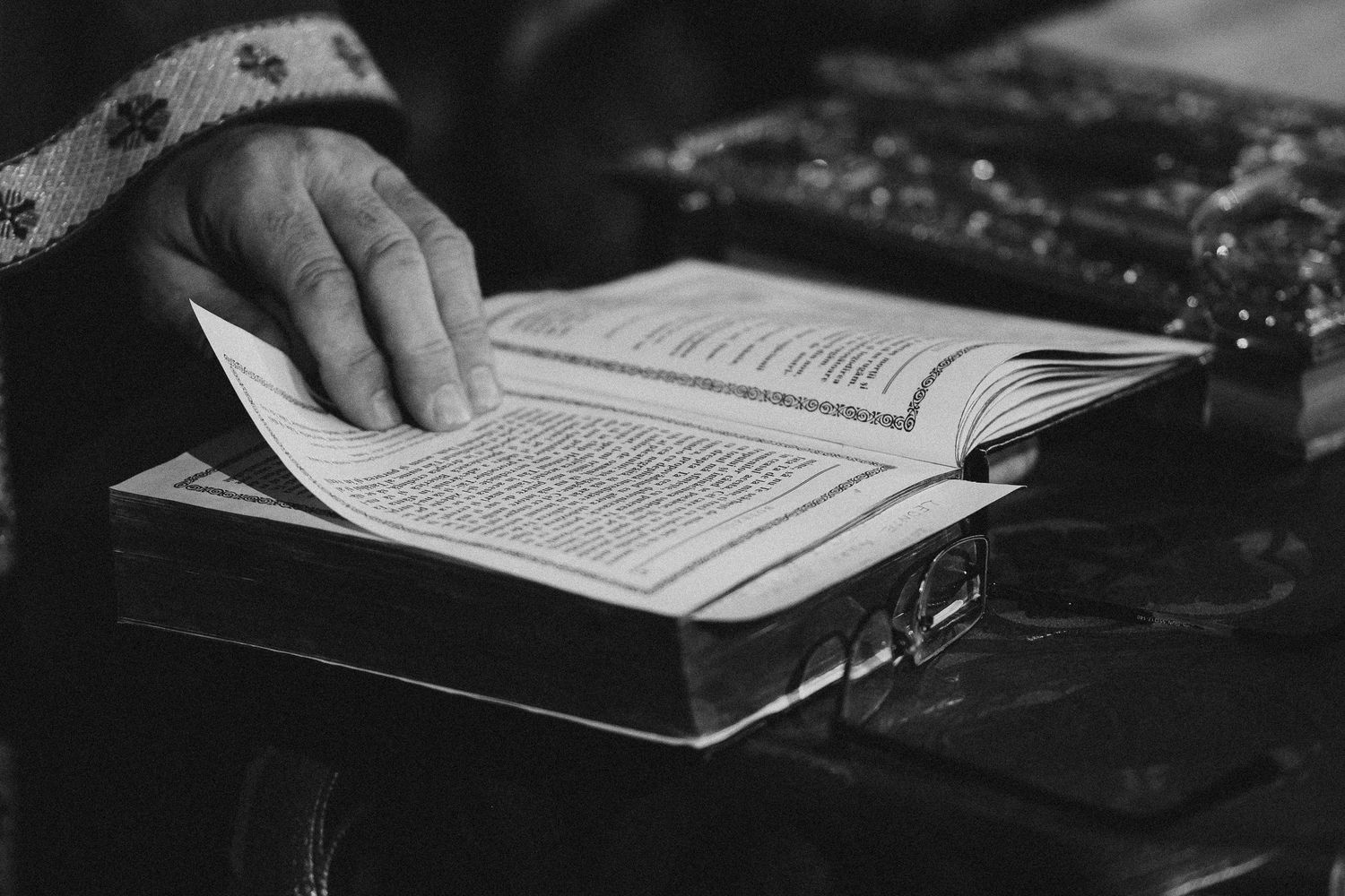 A hand turns pages of an open religious book resting on a wooden case in black and white.