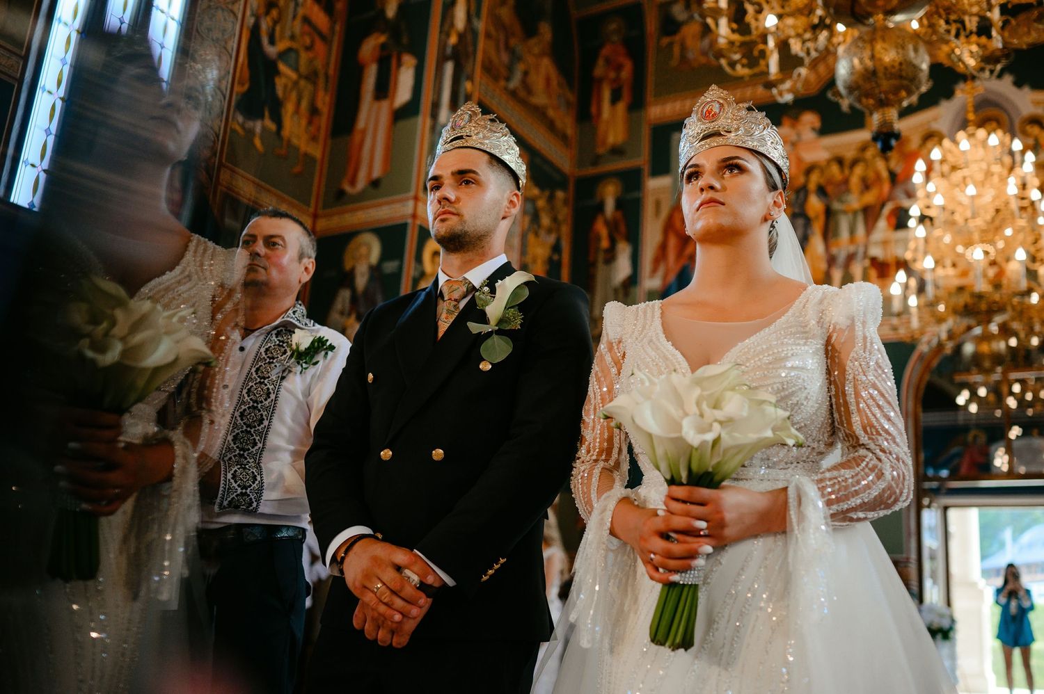 Bride and groom wearing traditional Orthodox wedding crowns during religious ceremony in ornate decorated church.