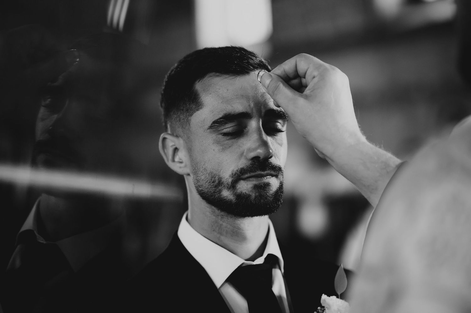 Black and white photo of groom receiving anointing on forehead during religious wedding ceremony.