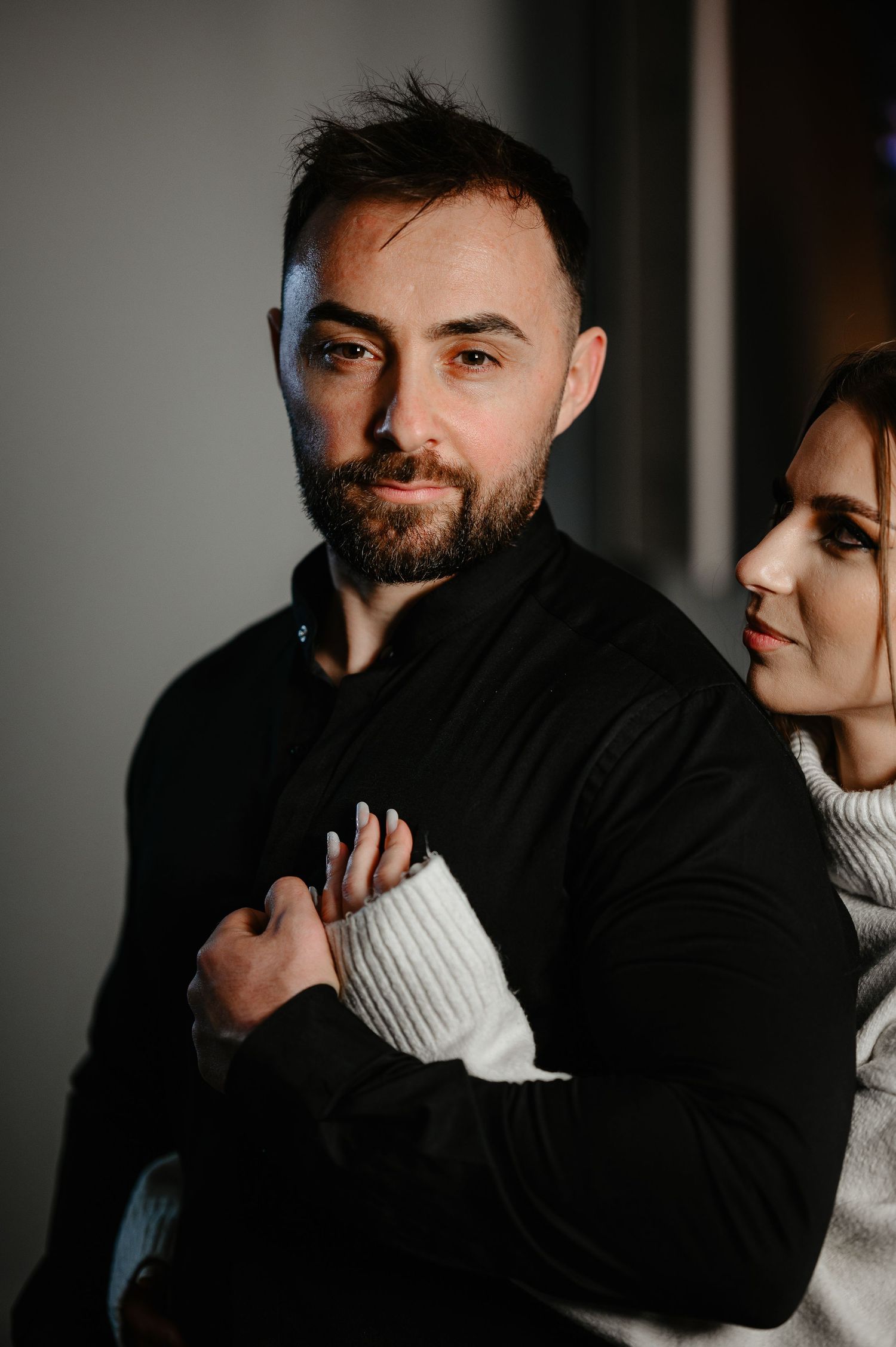 Bearded man in black shirt with woman in white sweater in moody portrait.