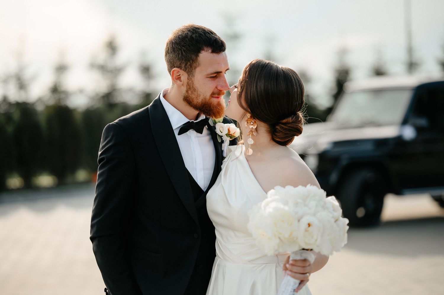 Wedding couple sharing romantic moment, groom in tuxedo, bride holding white floral bouquet.
