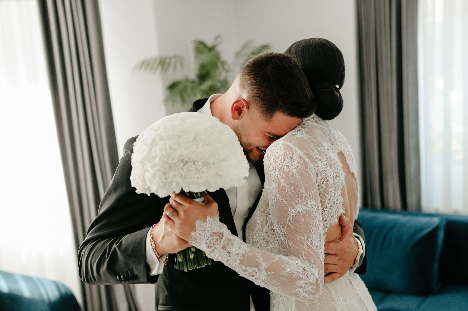 Groom embracing bride in elegant lace wedding dress during emotional first look reveal.