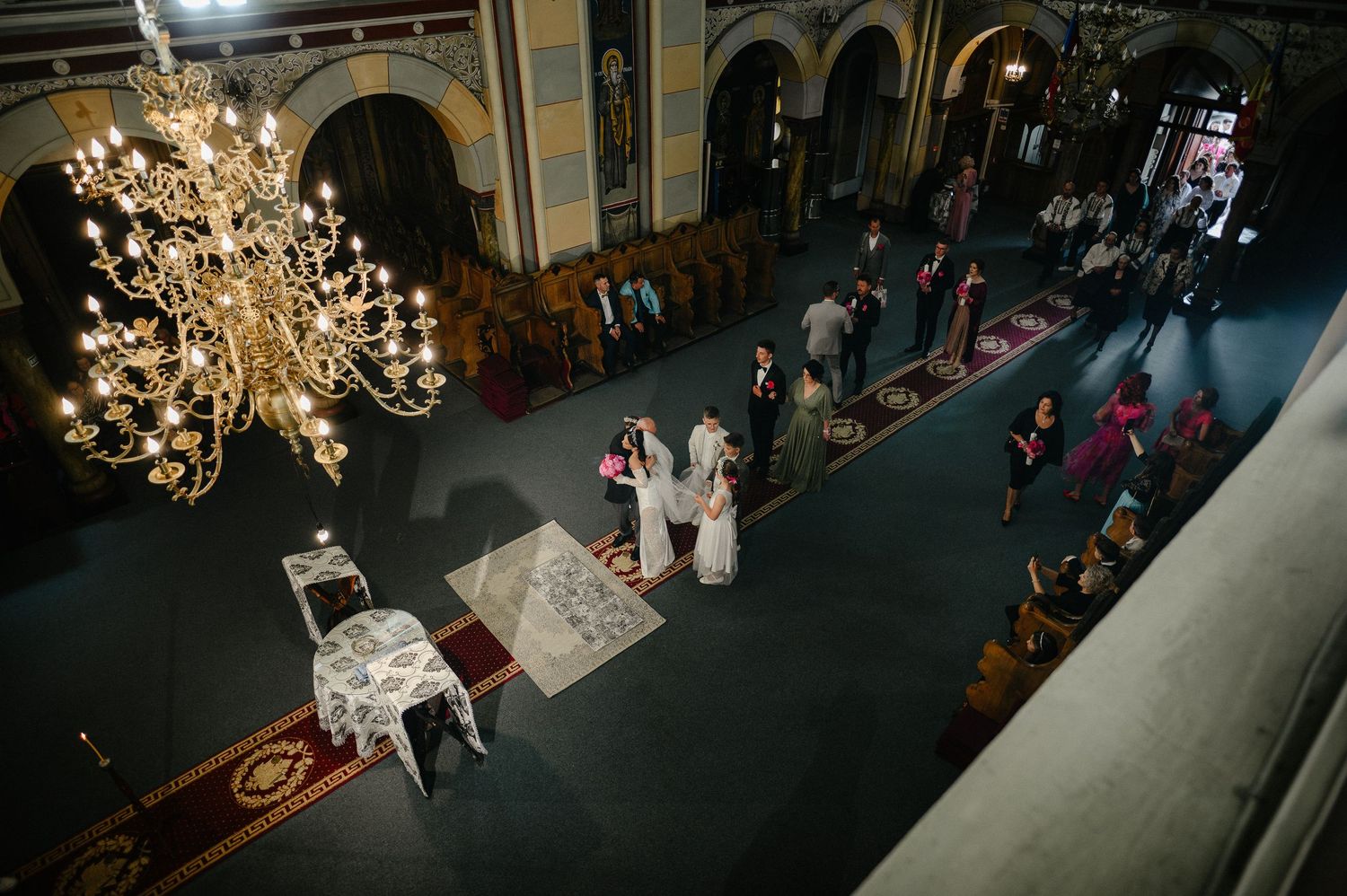 Aerial view of Orthodox church wedding ceremony with chandelier, guests seated in ornate interior.